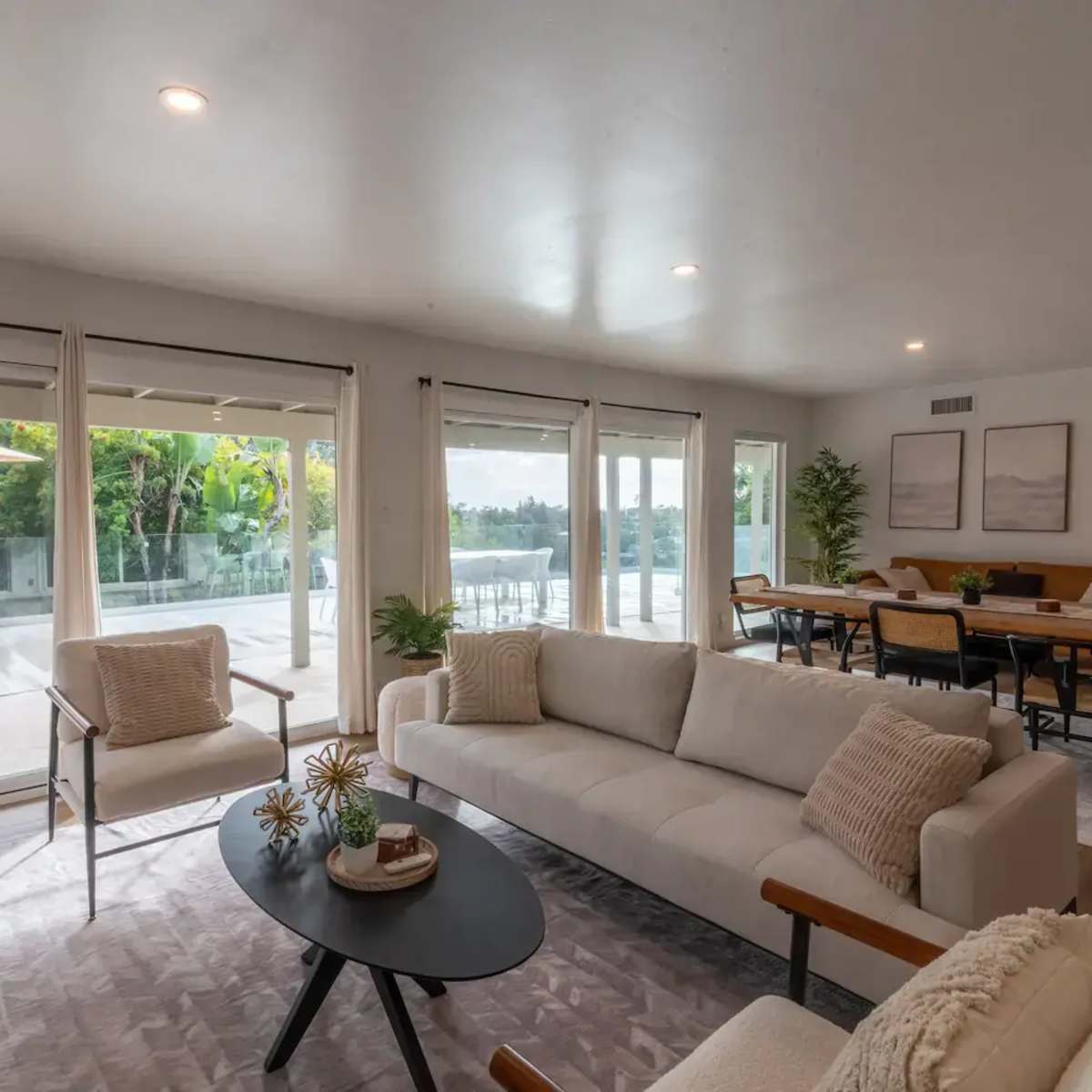 A modern living room with a light-colored sofa, a round coffee table, and large windows that provide a view of an outdoor area.