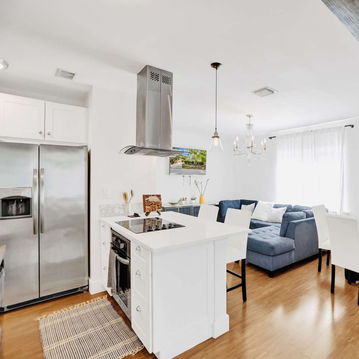 A modern kitchen and dining area with stainless steel appliances, a blue sectional sofa, a glass dining table, and hardwood flooring.