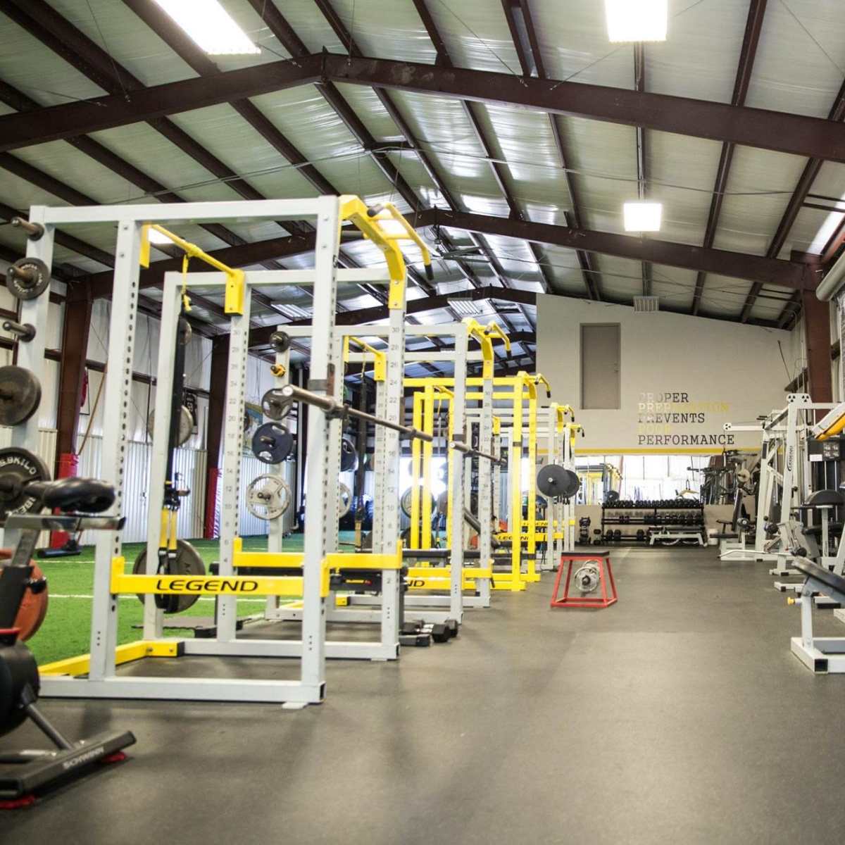 A spacious gym interior with various weightlifting and cardio equipment arranged in orderly rows beneath a high ceiling.