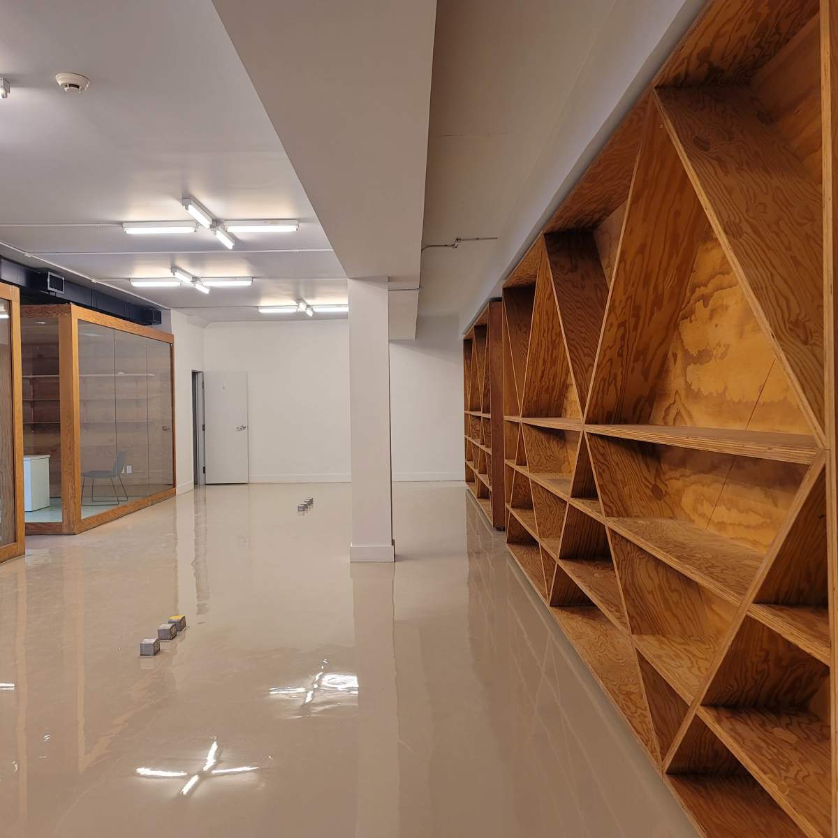 A spacious interior room with polished floors, wooden shelving units along one wall, and glass partitions separating additional areas.