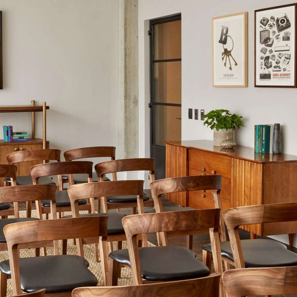 A meeting room is set up with wooden chairs facing a wall-mounted television and a sideboard displaying plants and books.