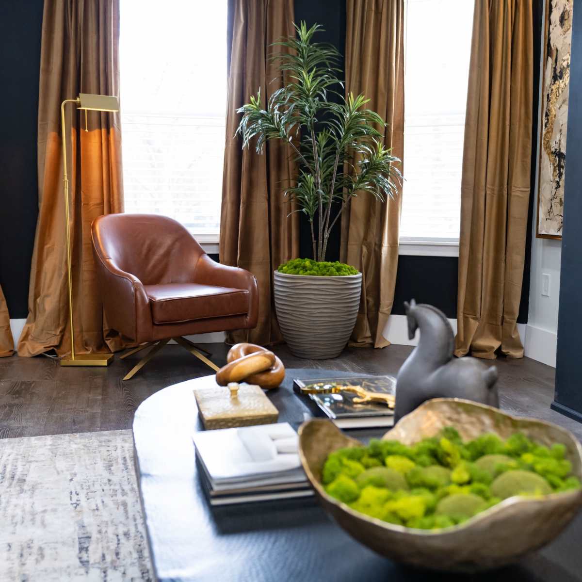 A cozy living room featuring a brown leather chair, a potted plant, and a coffee table adorned with decorative items and a bowl of green moss.