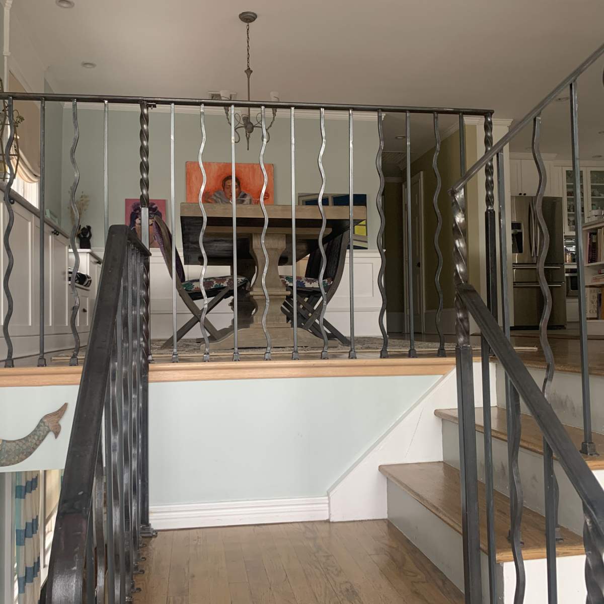 A staircase with a black railing leading to a dining area with a table and chairs, and a light fixture hanging above.