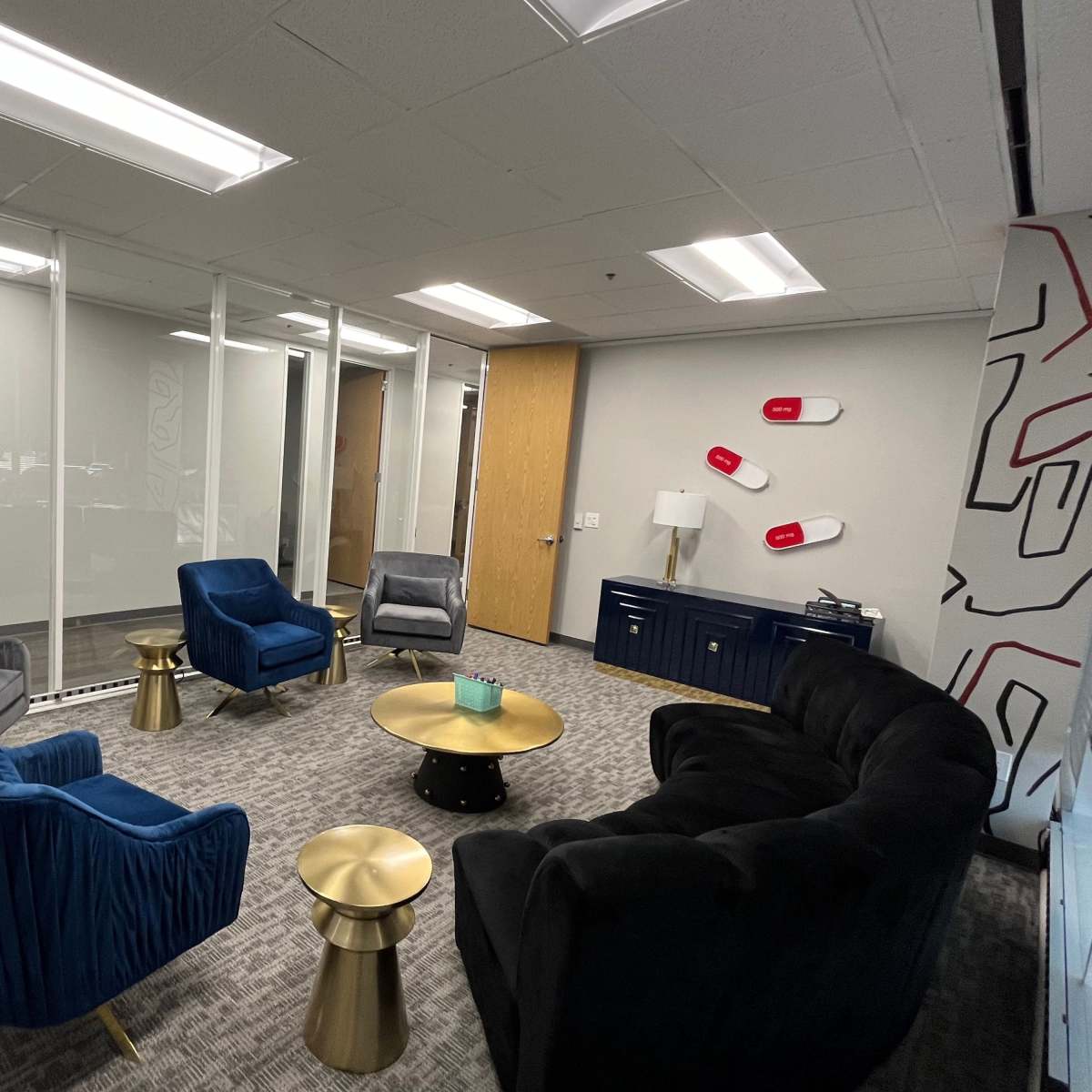 A modern office lounge area with a mix of upholstered seating, a small brass coffee table, and decorative elements against a neutral wall.