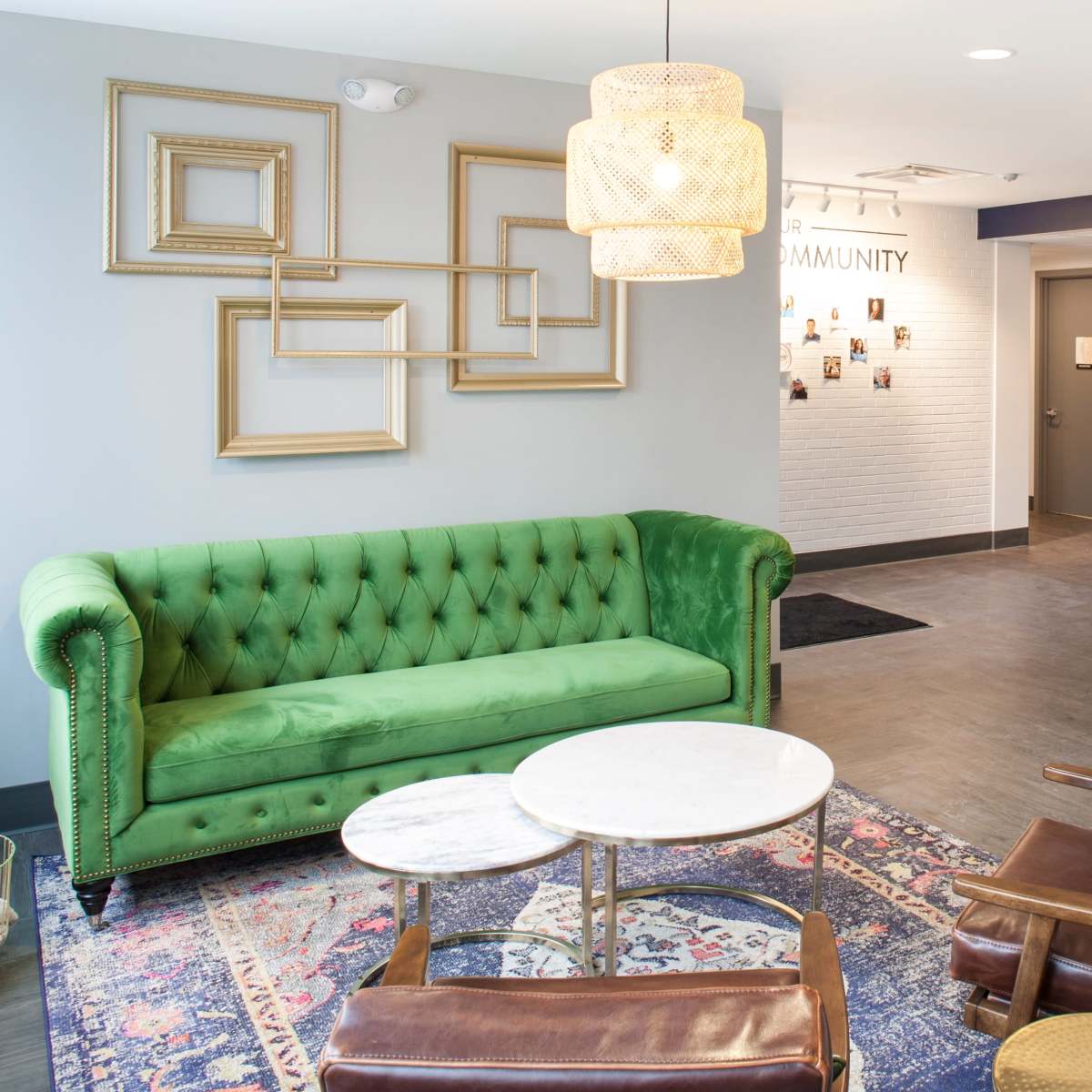 The scene depicts a modern lobby with a green tufted sofa, two brown armchairs, a marble-top coffee table, framed wall art, and a reception desk with a striped design.