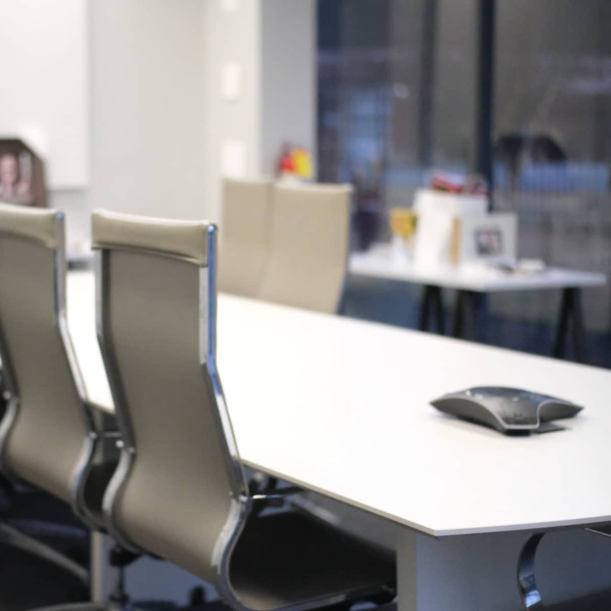 A modern conference room with a long table surrounded by several ergonomic chairs and a speakerphone on the table.
