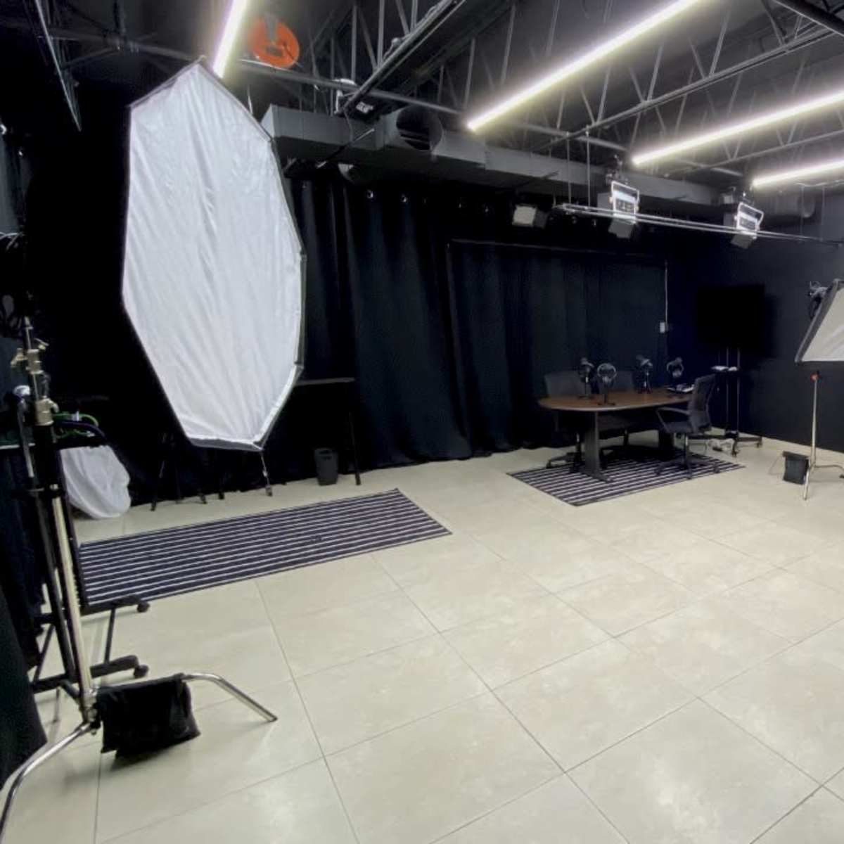 A photography studio featuring a central table, multiple lighting setups, and black curtains along the walls.