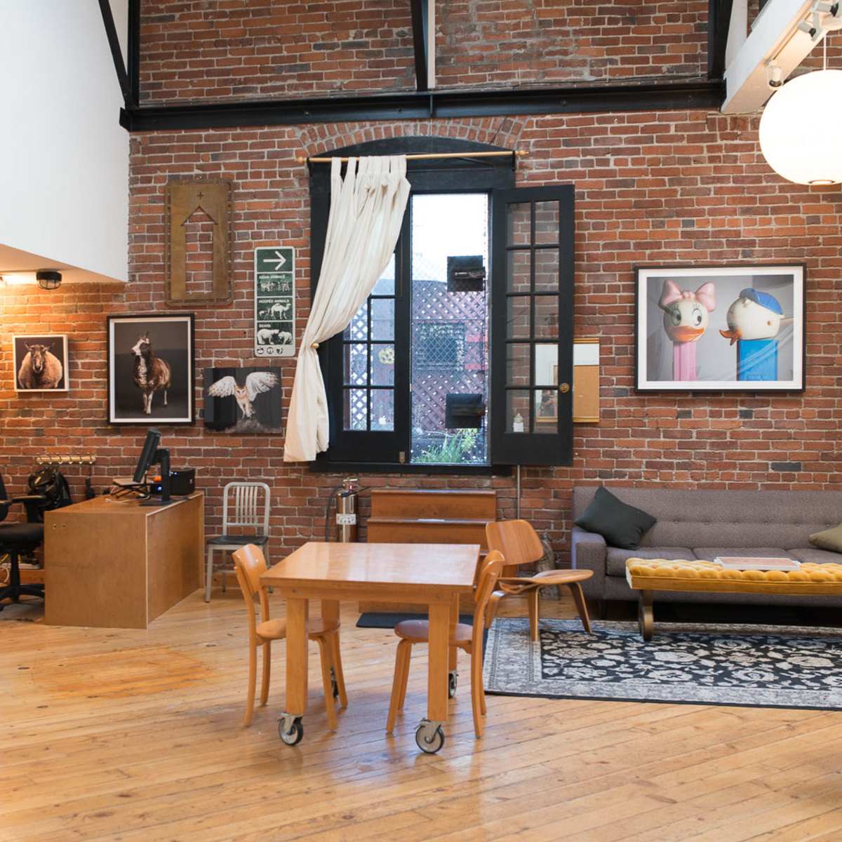 An interior of a spacious, contemporary room featuring exposed brick walls, a wooden table with chairs, and a workspace with a computer.