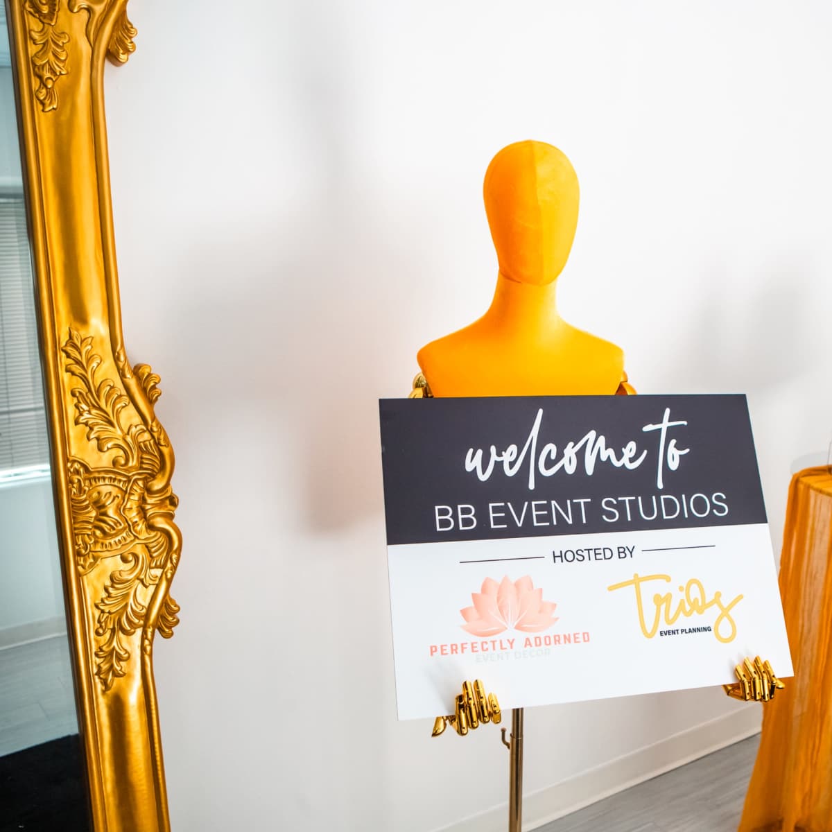 A bright orange mannequin displays a welcome sign for BB Event Studios in a well-lit room adorned with orange decorations.