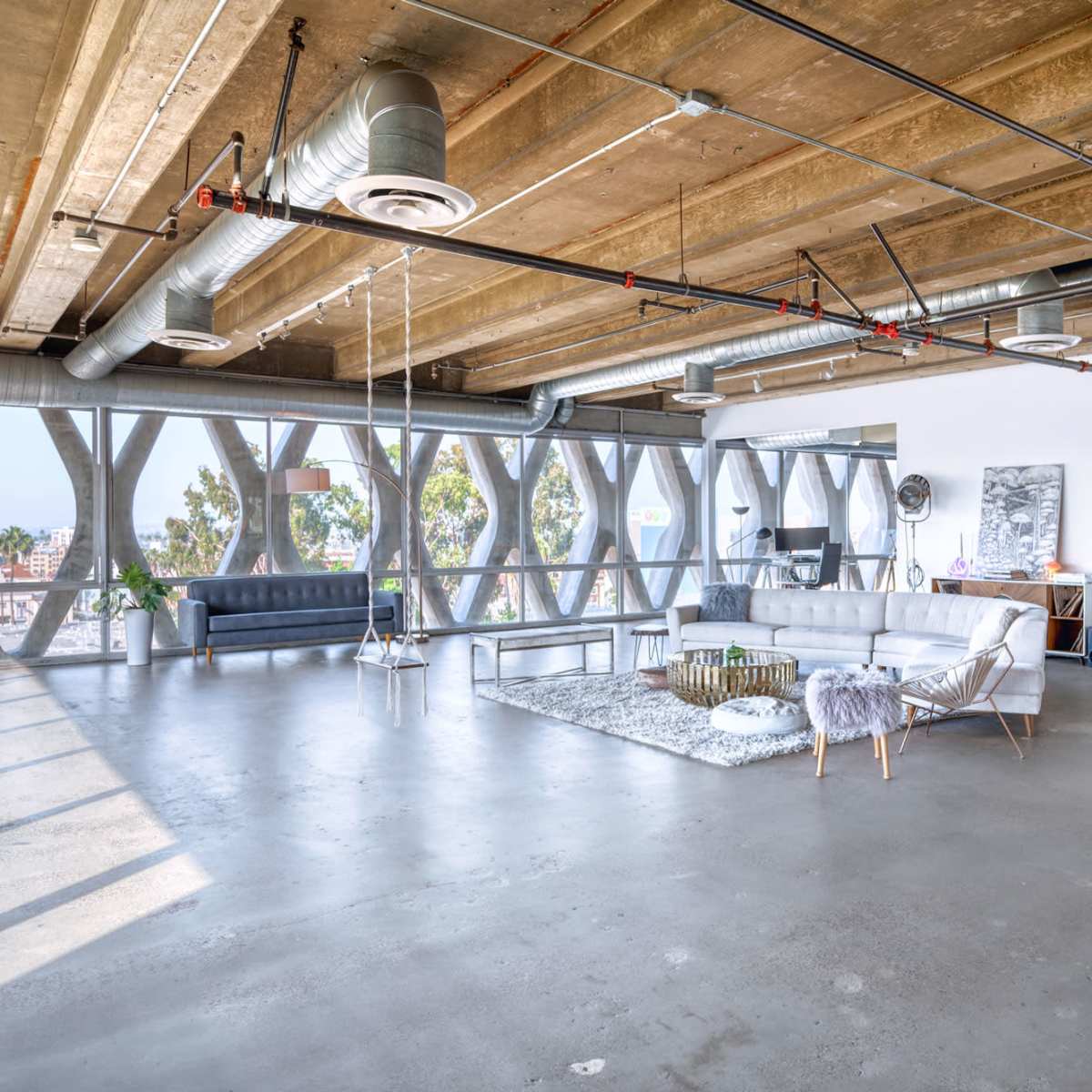 The spacious interior features industrial-style ceilings and large windows, creating an open area with modern furniture and a minimalist aesthetic.
