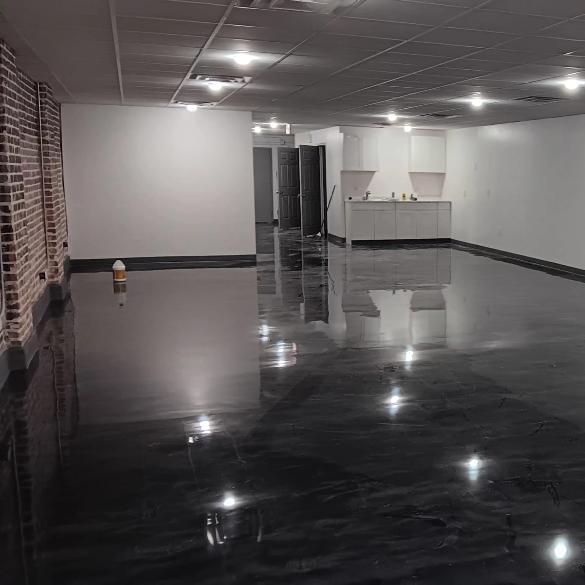 A large, vacant room with a polished black floor and a kitchenette area in the background.