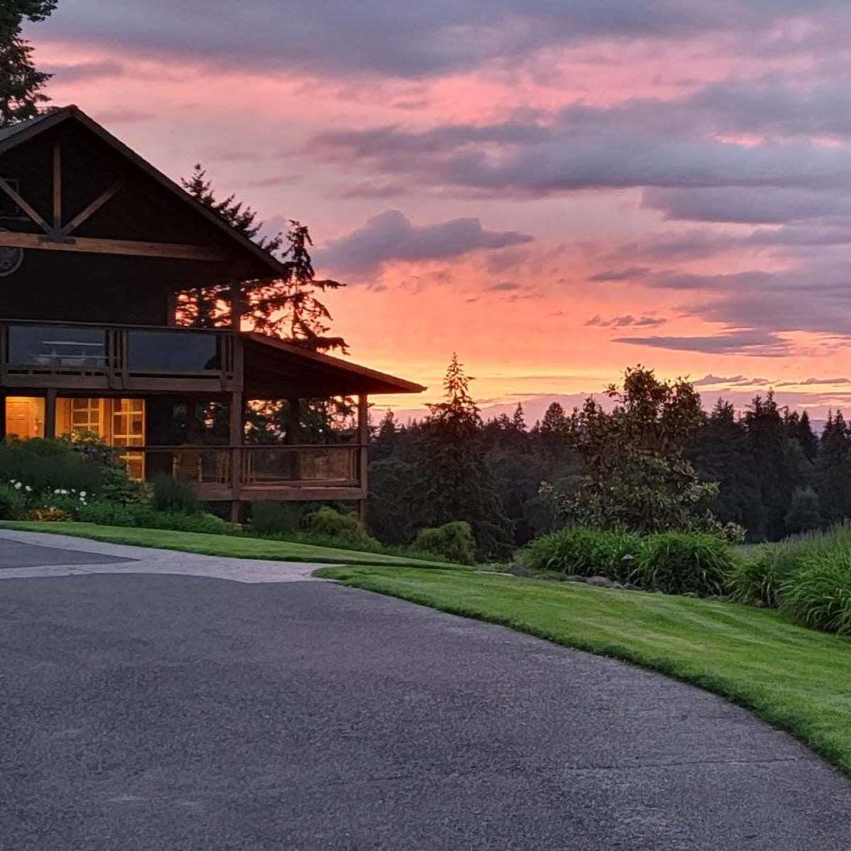 A couple walks along a pathway beside a vineyard at sunset, with a large house and lush greenery in the foreground.