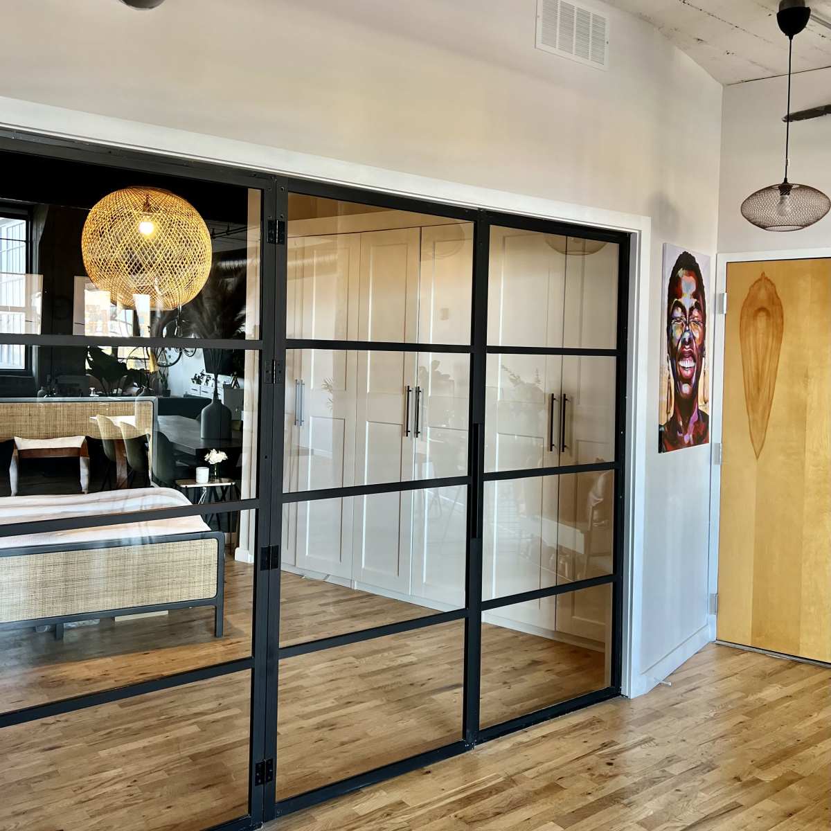 A modern interior space featuring a glass-paneled door leading to a bedroom with a stylish light fixture and a vibrant wall art piece.