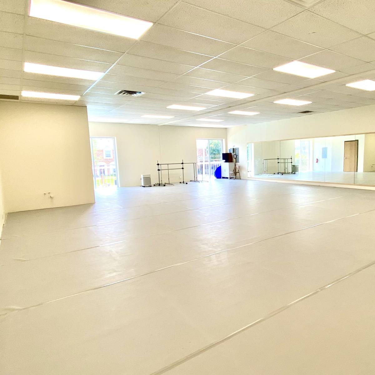An empty studio space features a mirrored wall, open floor, and bright overhead lighting.