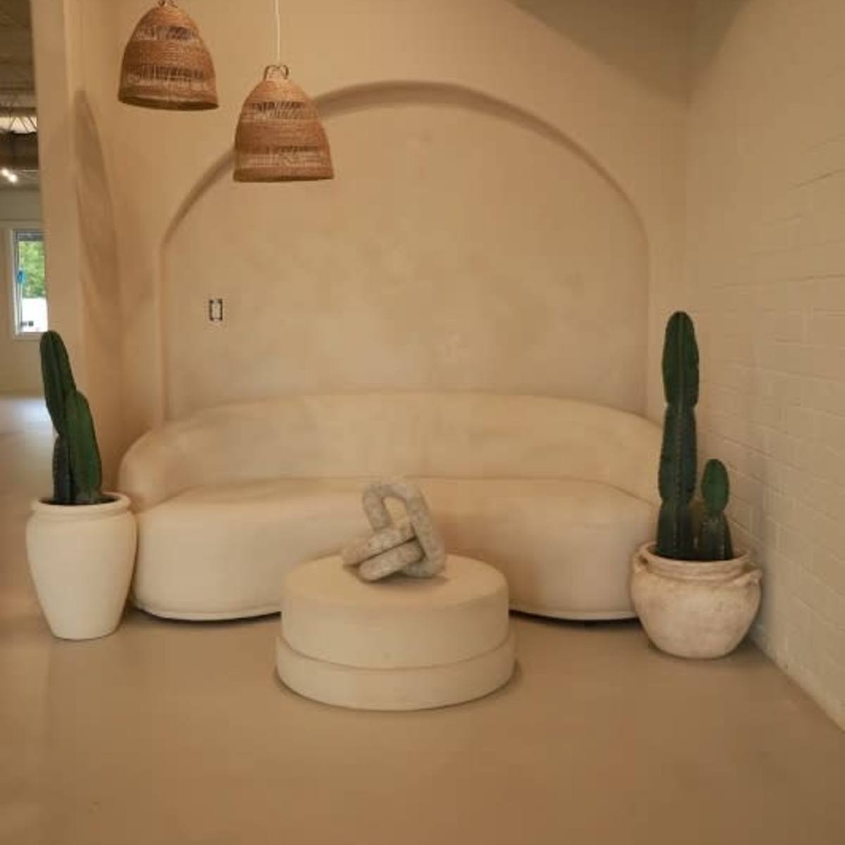 A curved, neutral-colored sofa is positioned in a minimalist setting, flanked by two potted cacti and a round coffee table.