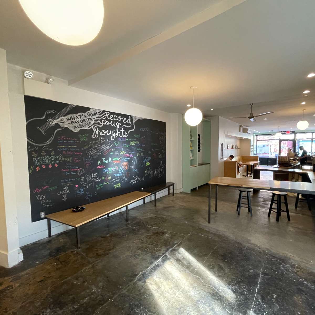 A spacious café interior featuring a large chalkboard wall with colorful writing and two wooden tables set up near the floor.