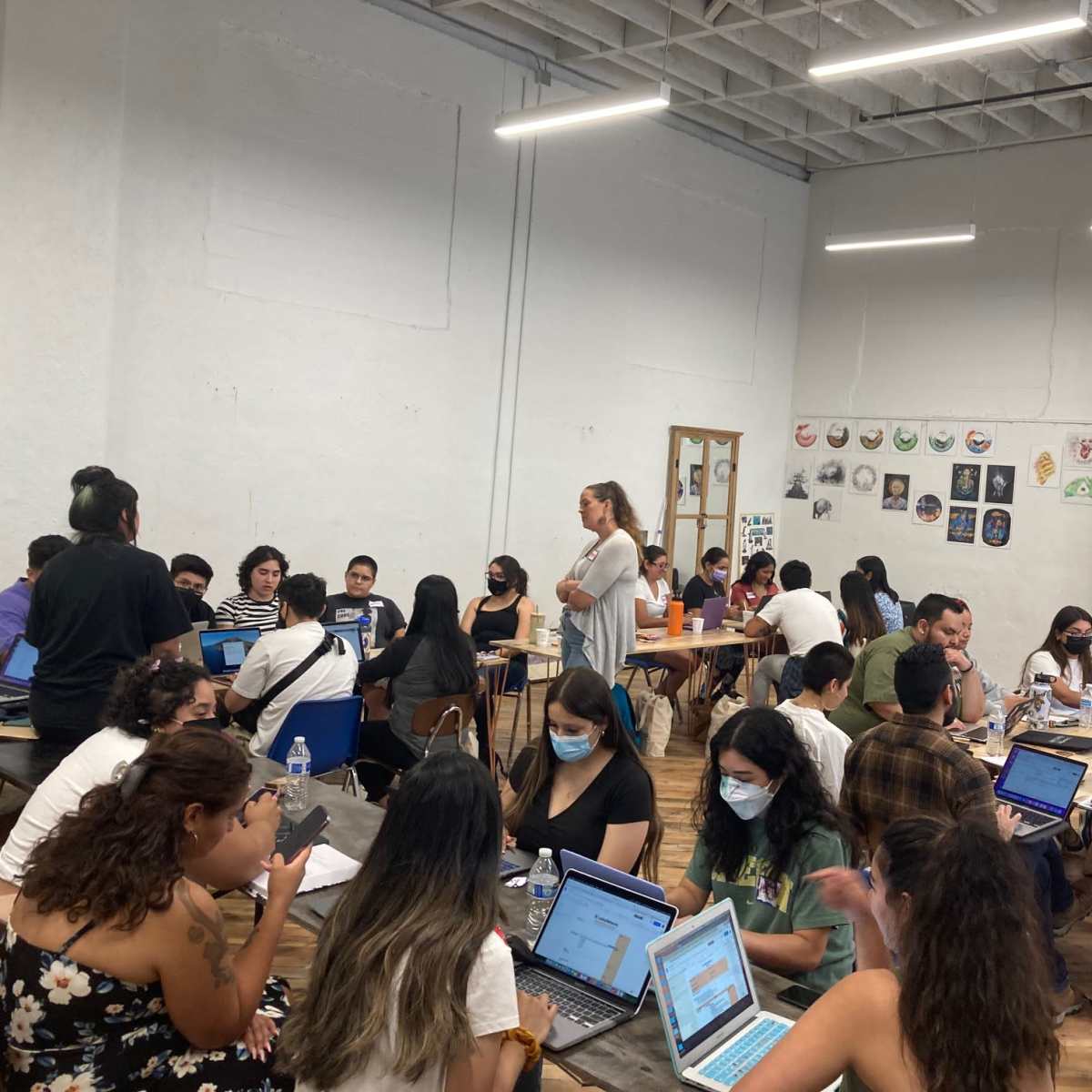 A diverse group of people is engaged in collaborative work at tables in a well-lit room with various artworks displayed on the walls.