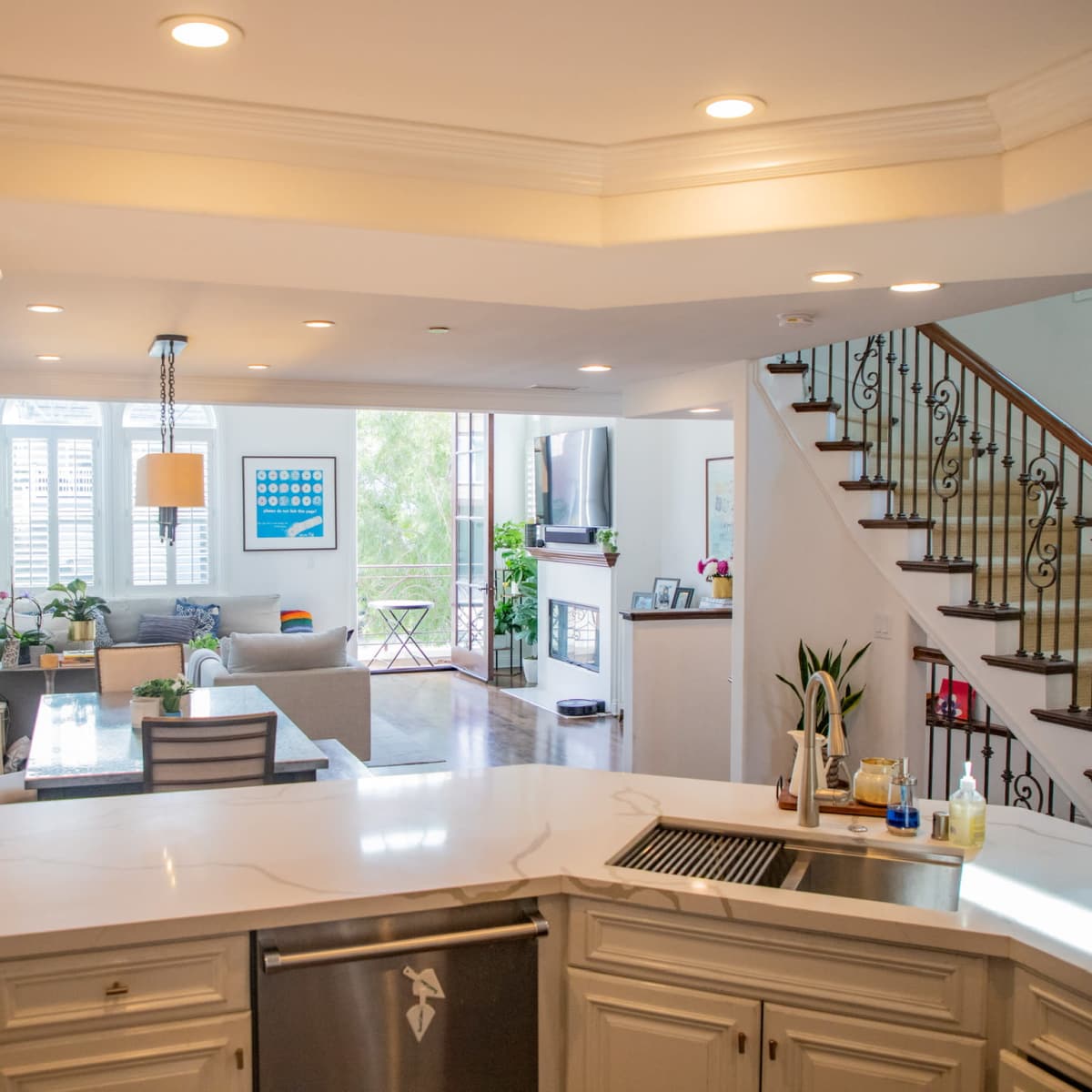 A modern open-concept kitchen with a marble countertop that overlooks a living area and a staircase.