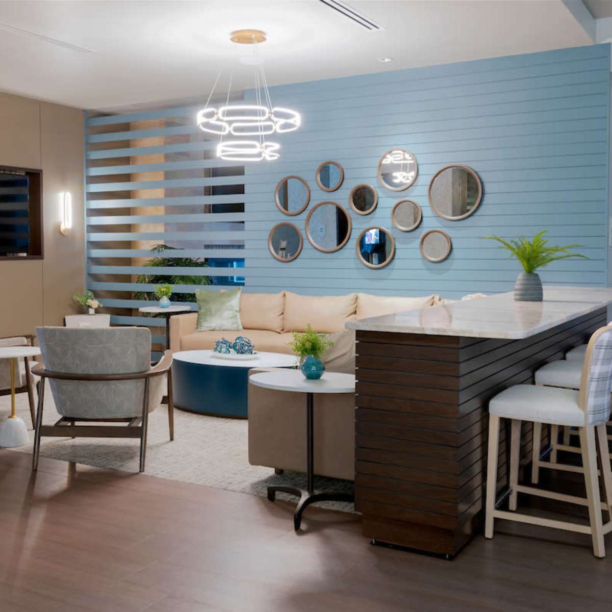 A modern living area featuring a sectional sofa, a bar counter with stools, and various decor elements, including a cluster of mirrors on a light blue wall.