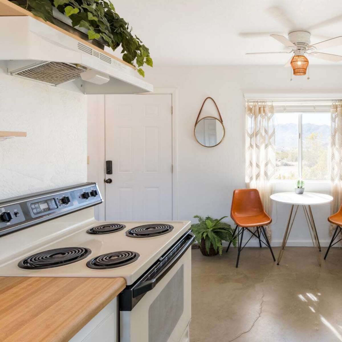 A kitchen features a stove, a retro-style fridge, two chairs at a small table, and a window with scenic views.