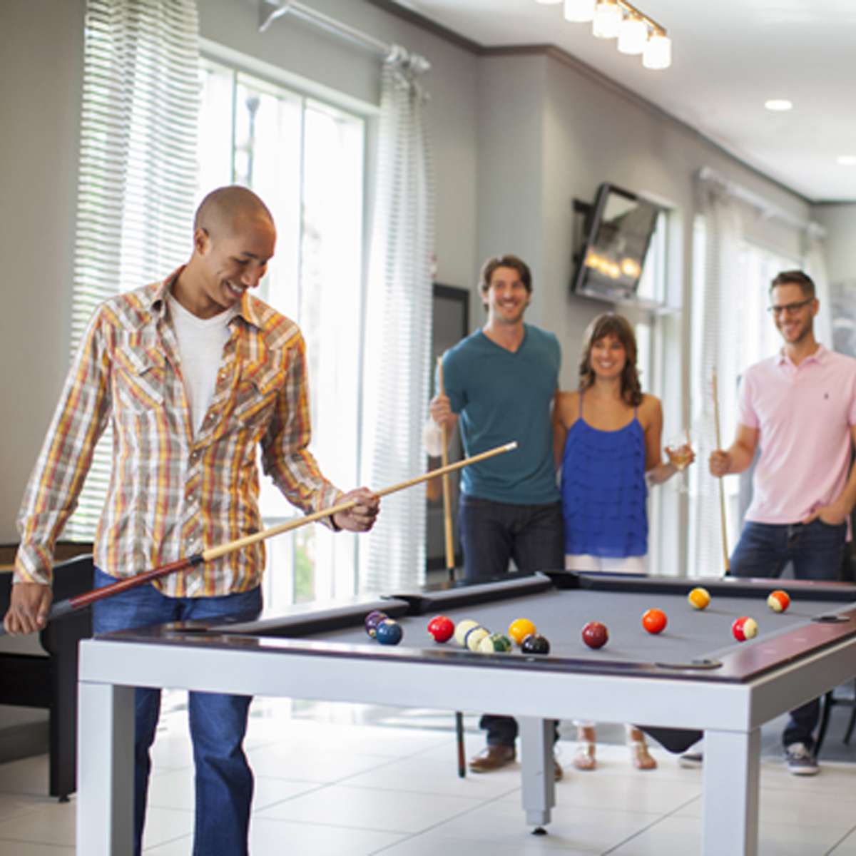 A group of four people socialize in a recreational area while one person prepares to take a shot at a pool table.