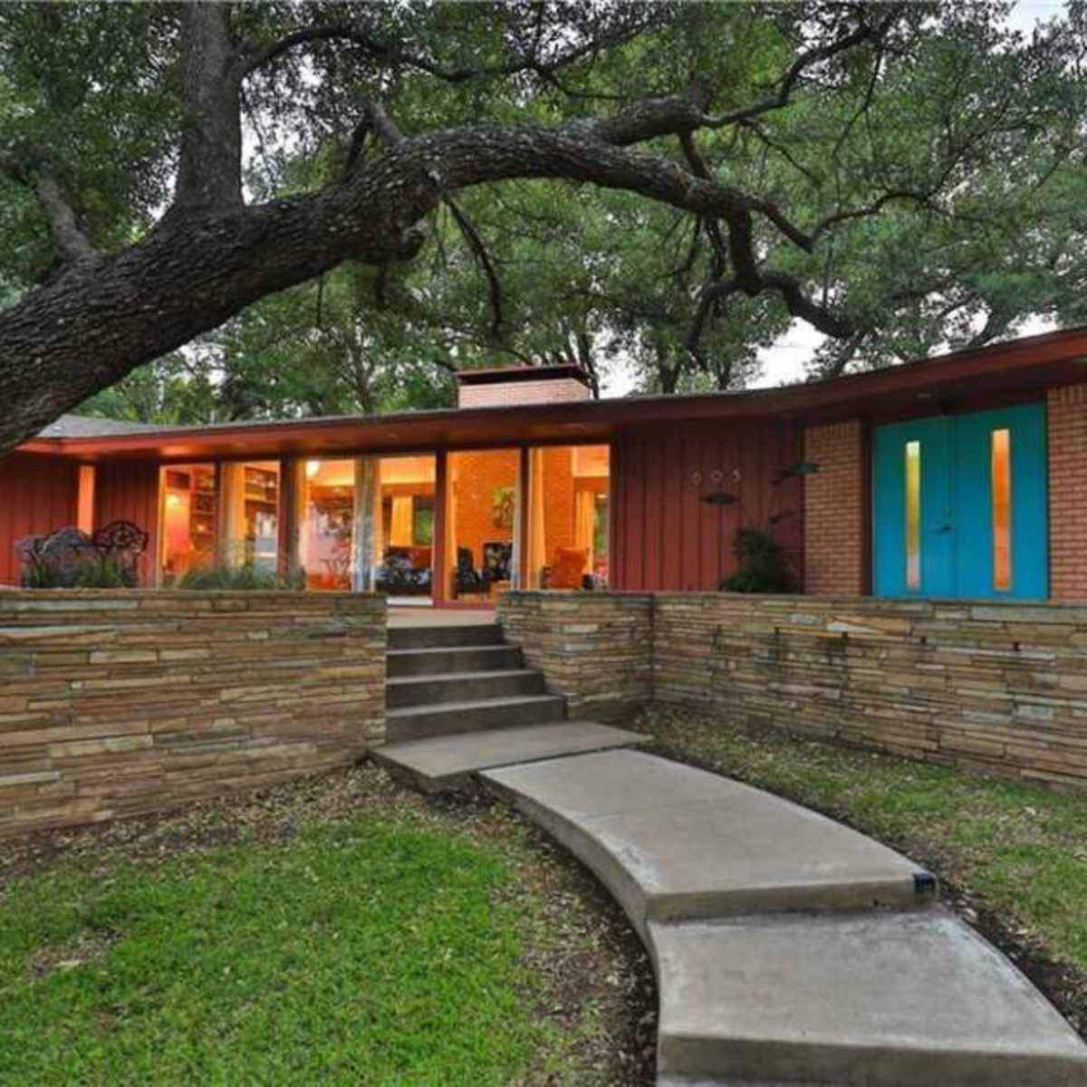 A modern home with large windows and a stone walkway is set among lush greenery.