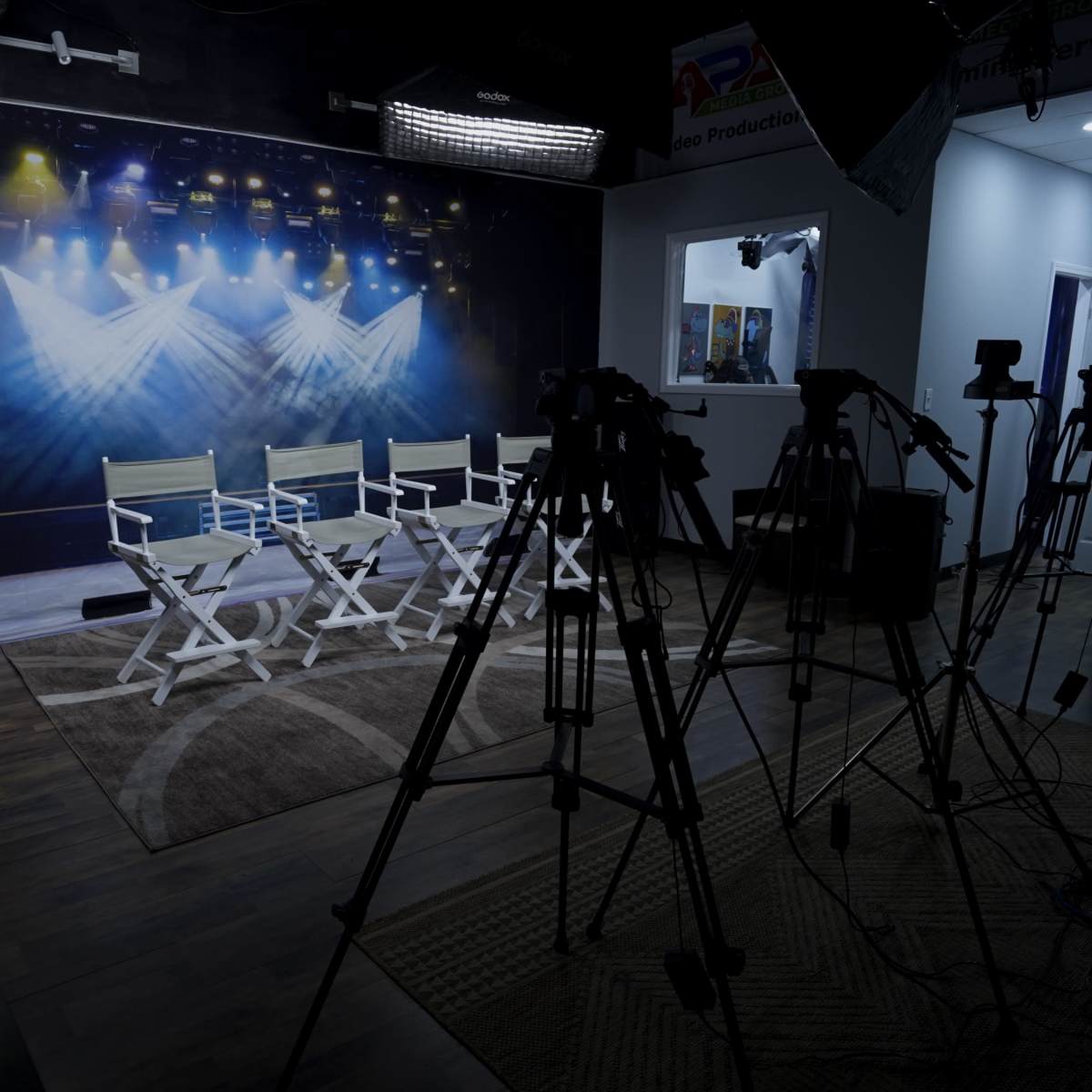 A studio setup with four empty director's chairs and several tripods positioned in front of a backdrop featuring stage lighting.