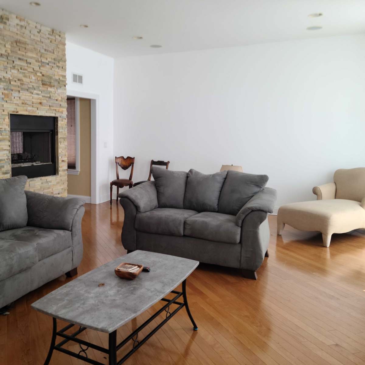 A living room with two gray sofas, a stone fireplace, a coffee table, and a light-colored chair in the corner.