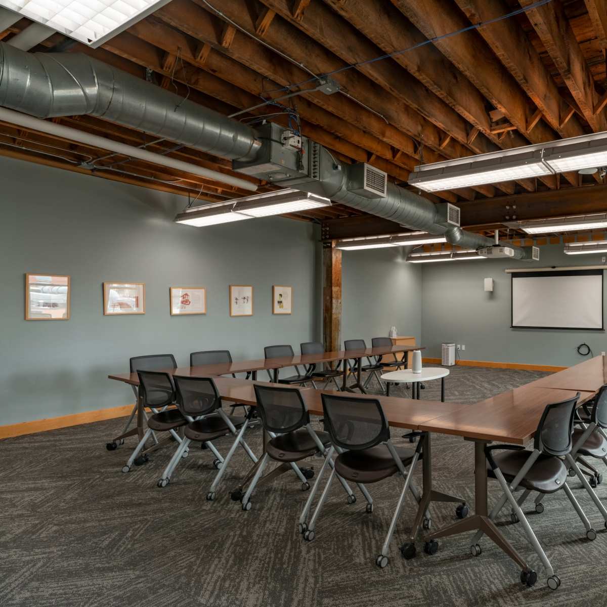 A spacious conference room features a large, rectangular table surrounded by rolling chairs, with exposed wooden beams and brick walls.