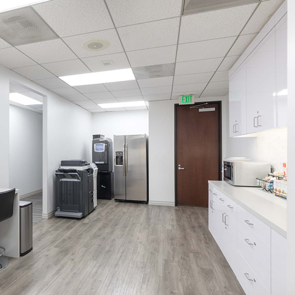 A modern break room equipped with a refrigerator, microwave, and snack area, featuring a table and chairs, and a colorful painting on the wall.