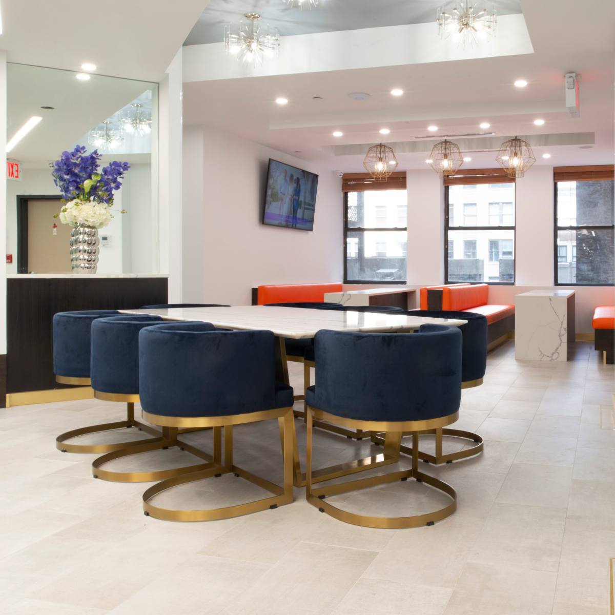 The scene shows a modern dining area featuring a round table surrounded by navy blue upholstered chairs, complemented by orange and gray seating along the walls.