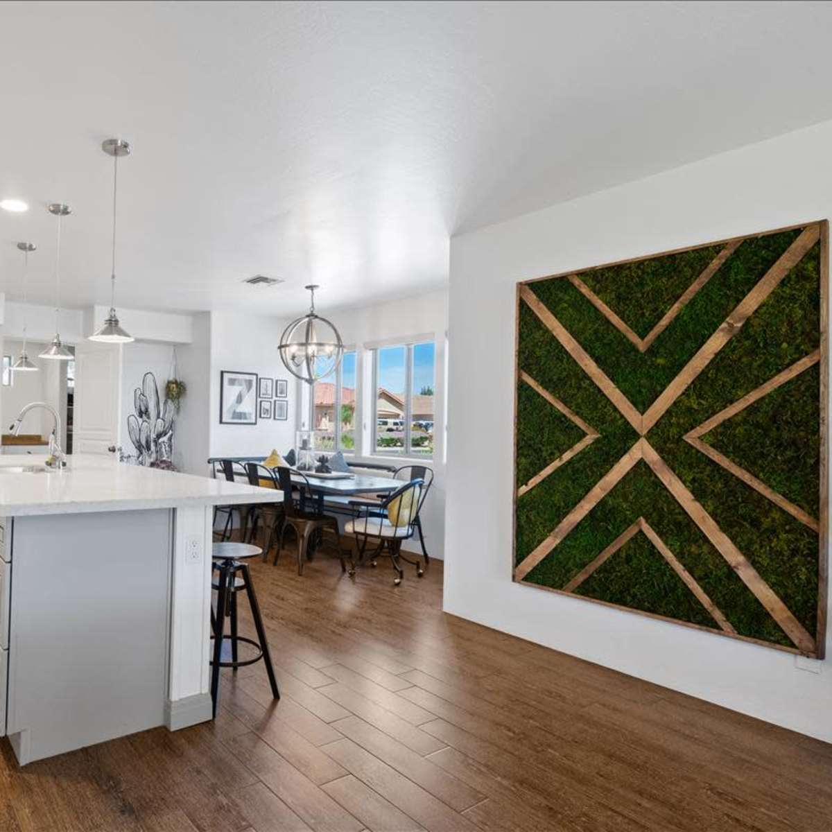 A modern kitchen with white cabinetry, stainless steel appliances, and a dining area featuring a table and chairs near a decorative wall with a green vertical design.