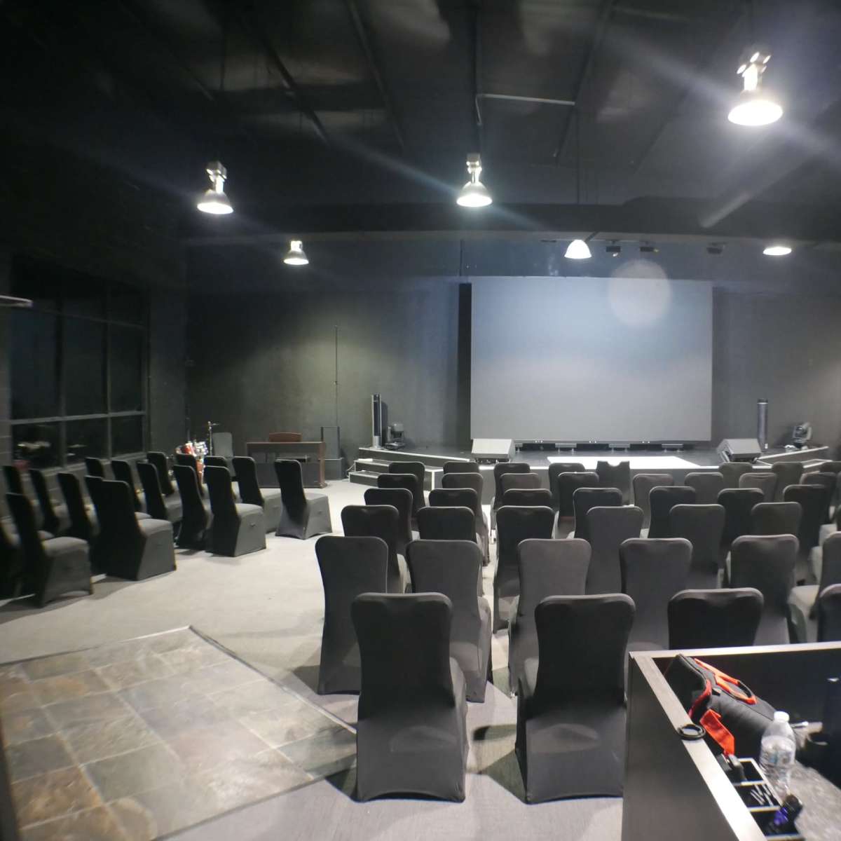 An empty auditorium with rows of black chairs facing a large projection screen.