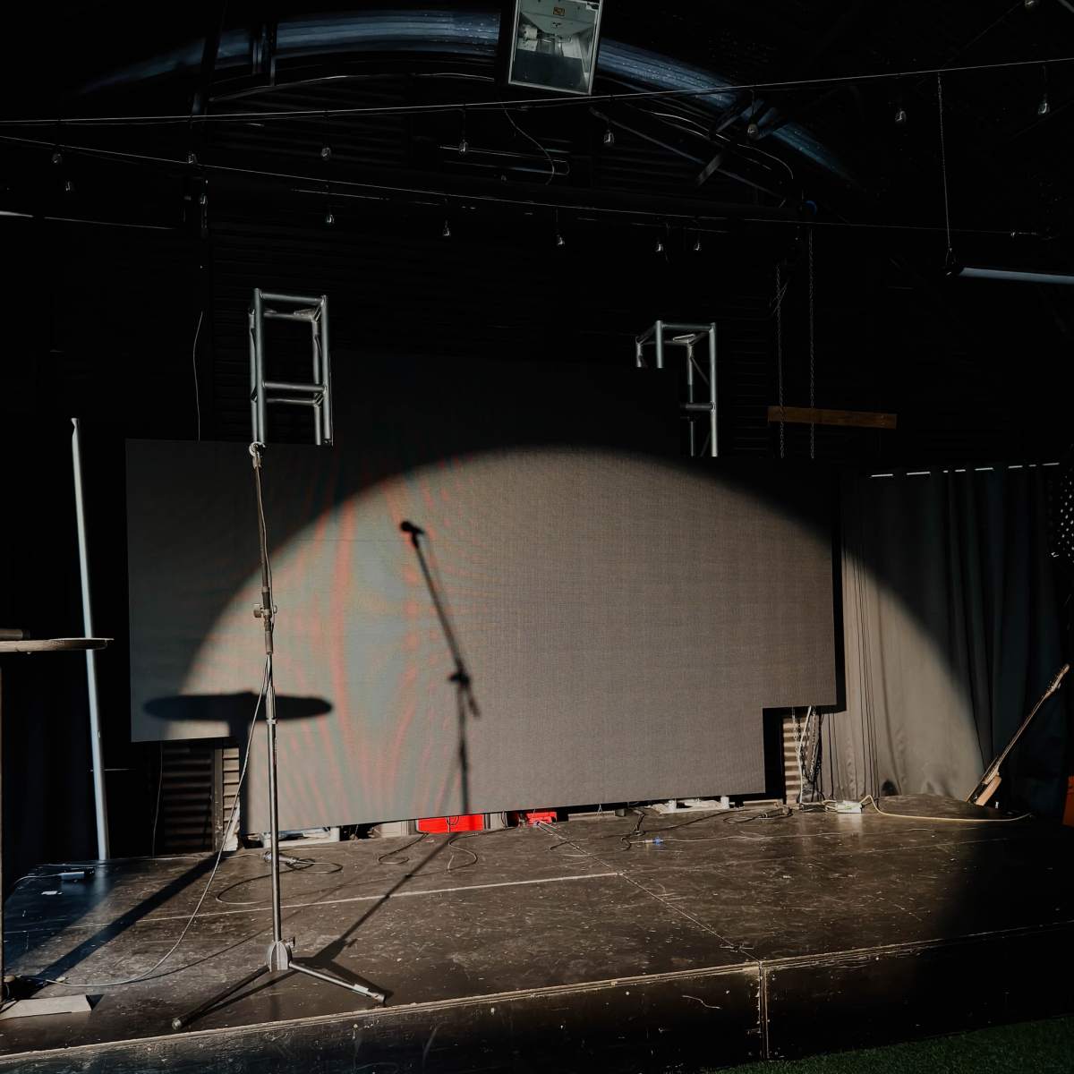 A microphone stand is positioned in front of a large blank screen on a dimly lit stage.
