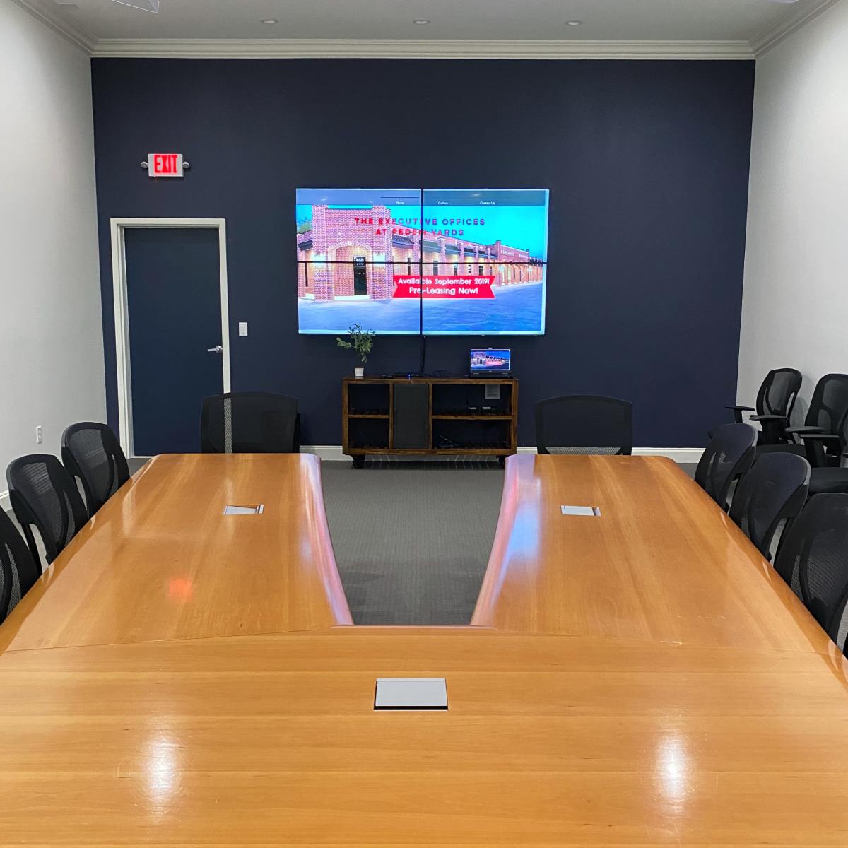 A large conference room features a long wooden table facing a mounted screen with a presentation.