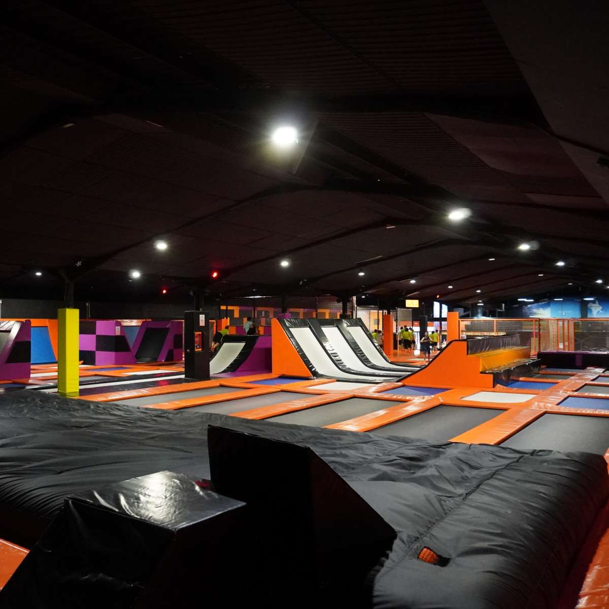 A large indoor trampoline park with multiple trampolines, foam pits, and an open play area under low lighting.