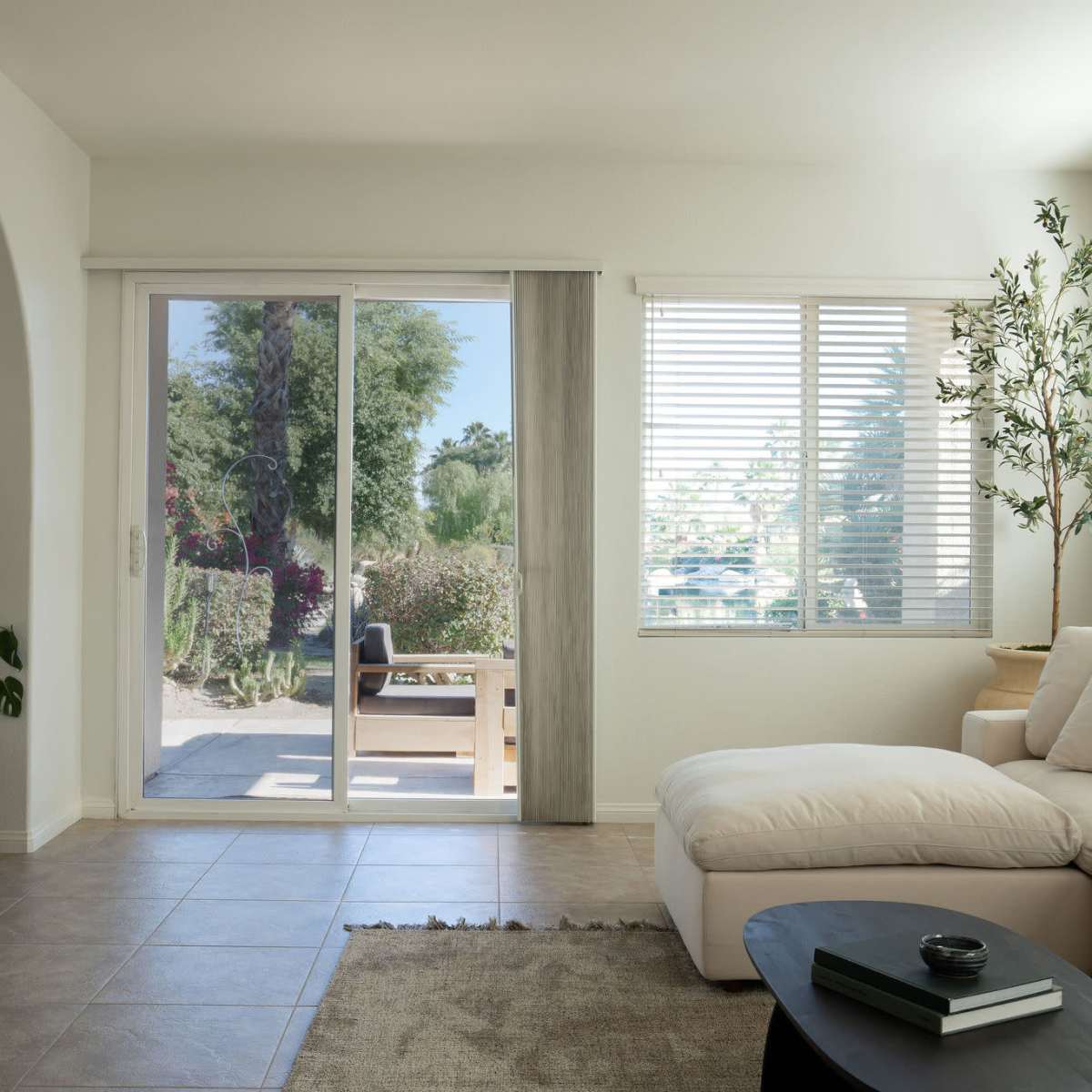 A bright living room with a white sectional sofa, a black coffee table, and large sliding glass doors leading to an outdoor patio.