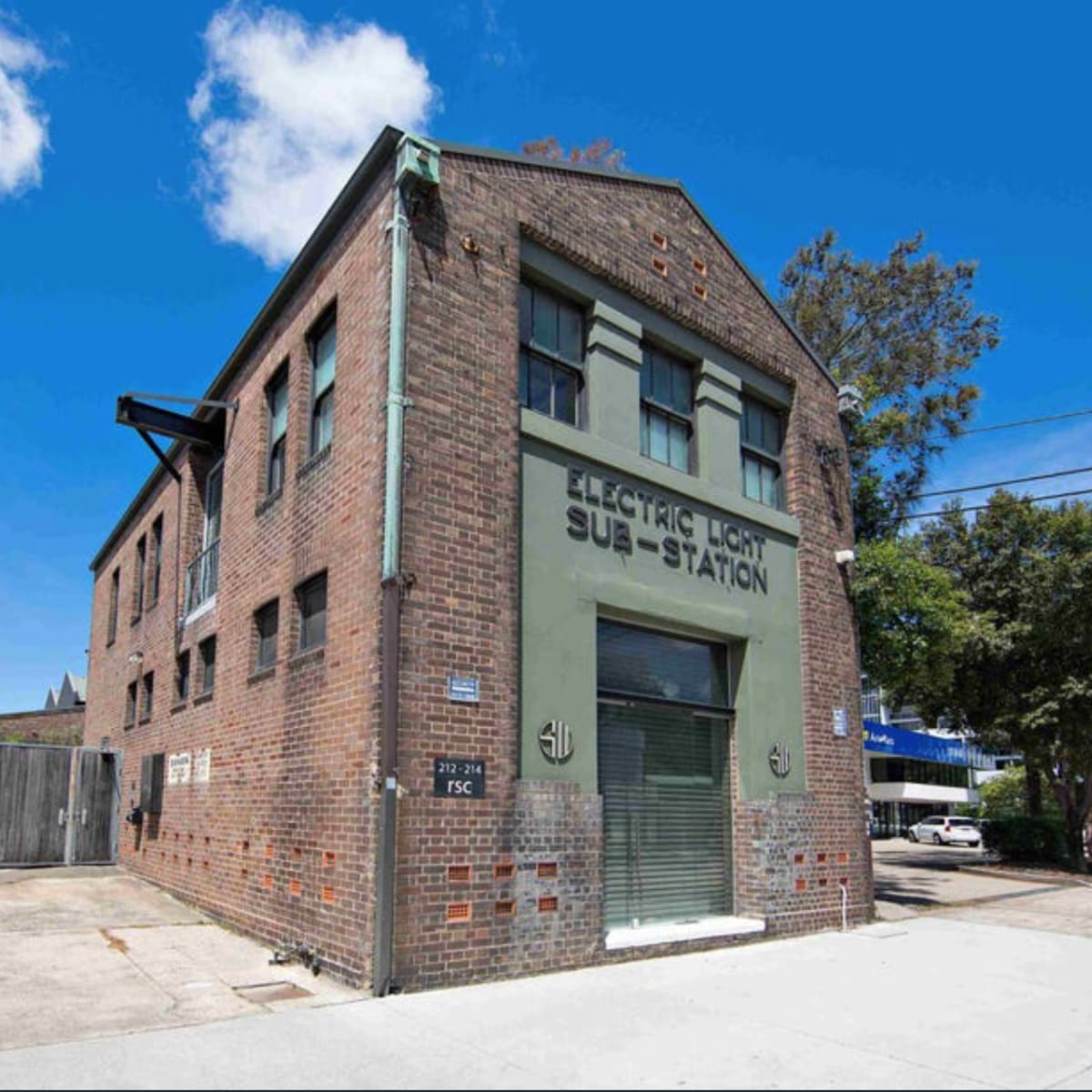 A two-story brick building labeled "ELECTRIC LIGHT SUB-STATION," with green detailing and a clear blue sky overhead.