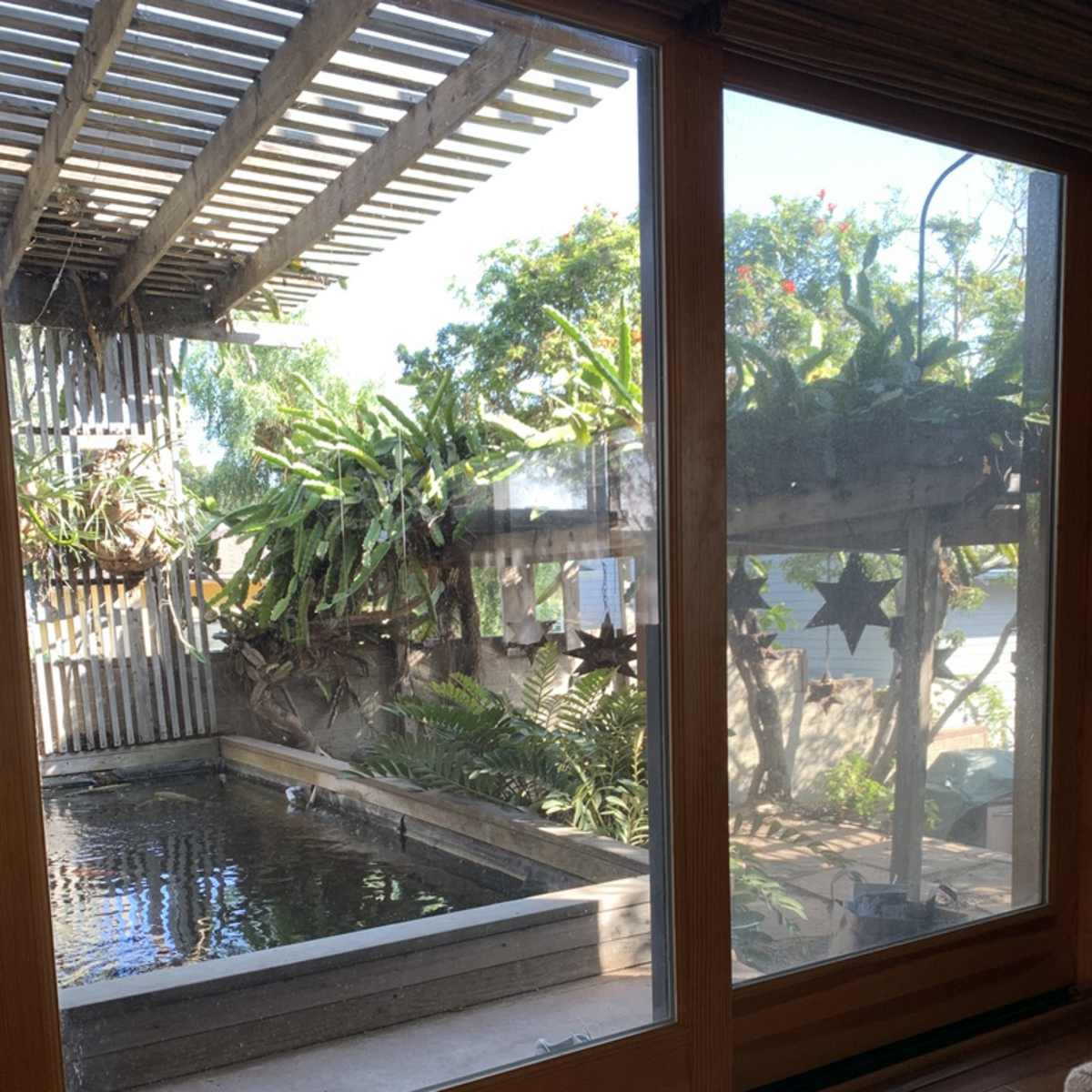 A large glass window overlooking a serene outdoor space with a pond, greenery, and wooden structures.