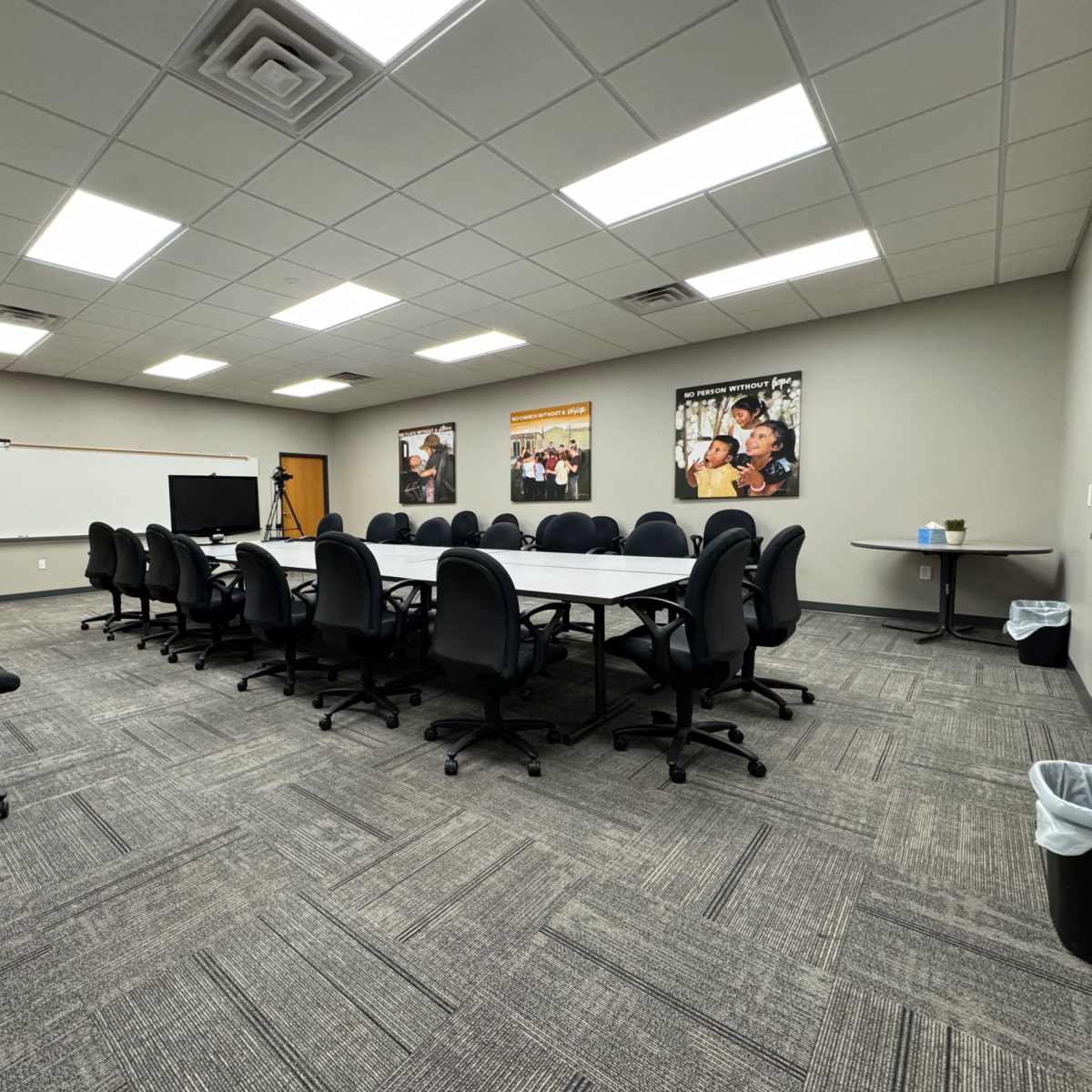 A spacious conference room with a large rectangular table surrounded by black office chairs, and photographs on the walls.