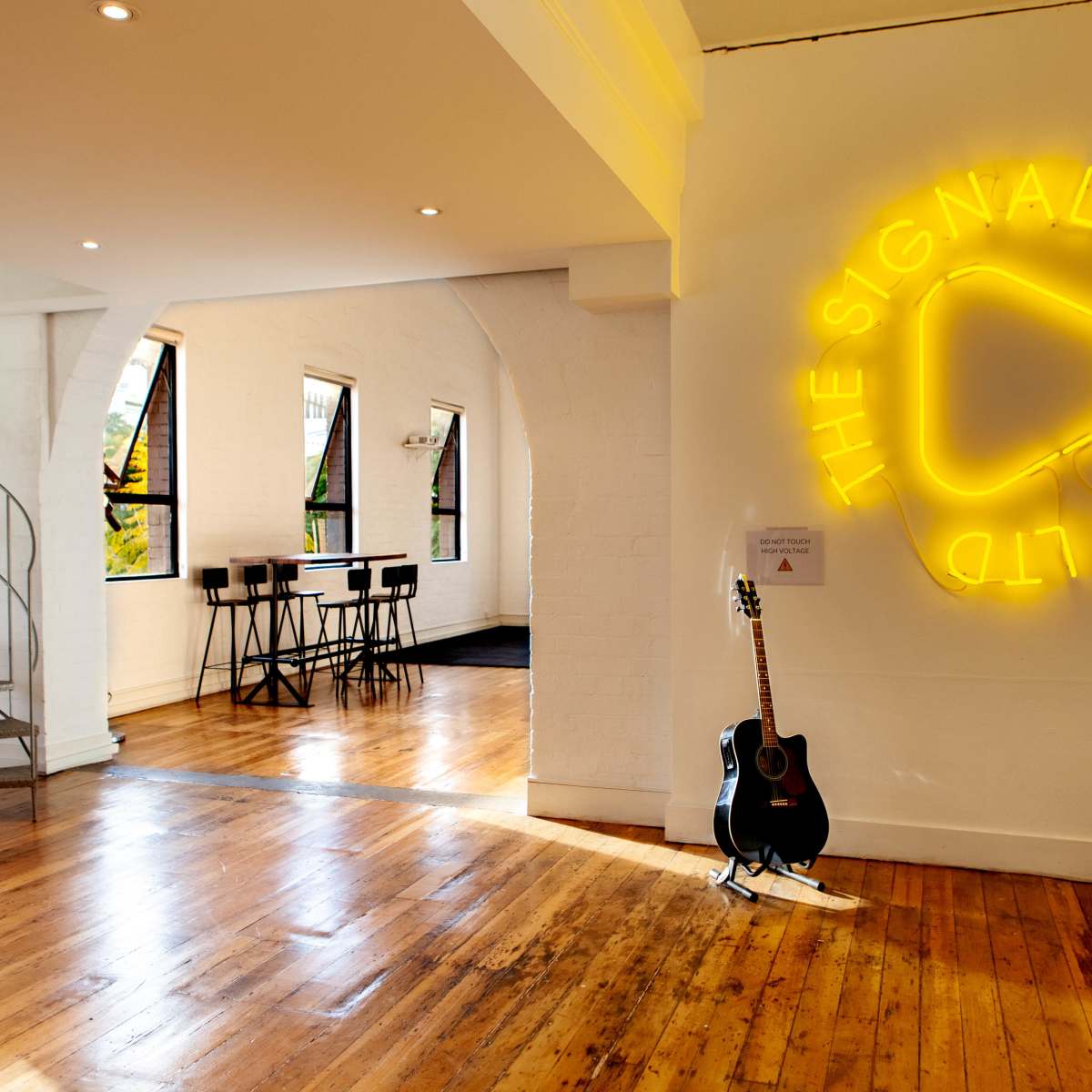 The interior features a spiral staircase, a neon sign on the wall, and a guitar leaning against the wall with wooden flooring throughout.
