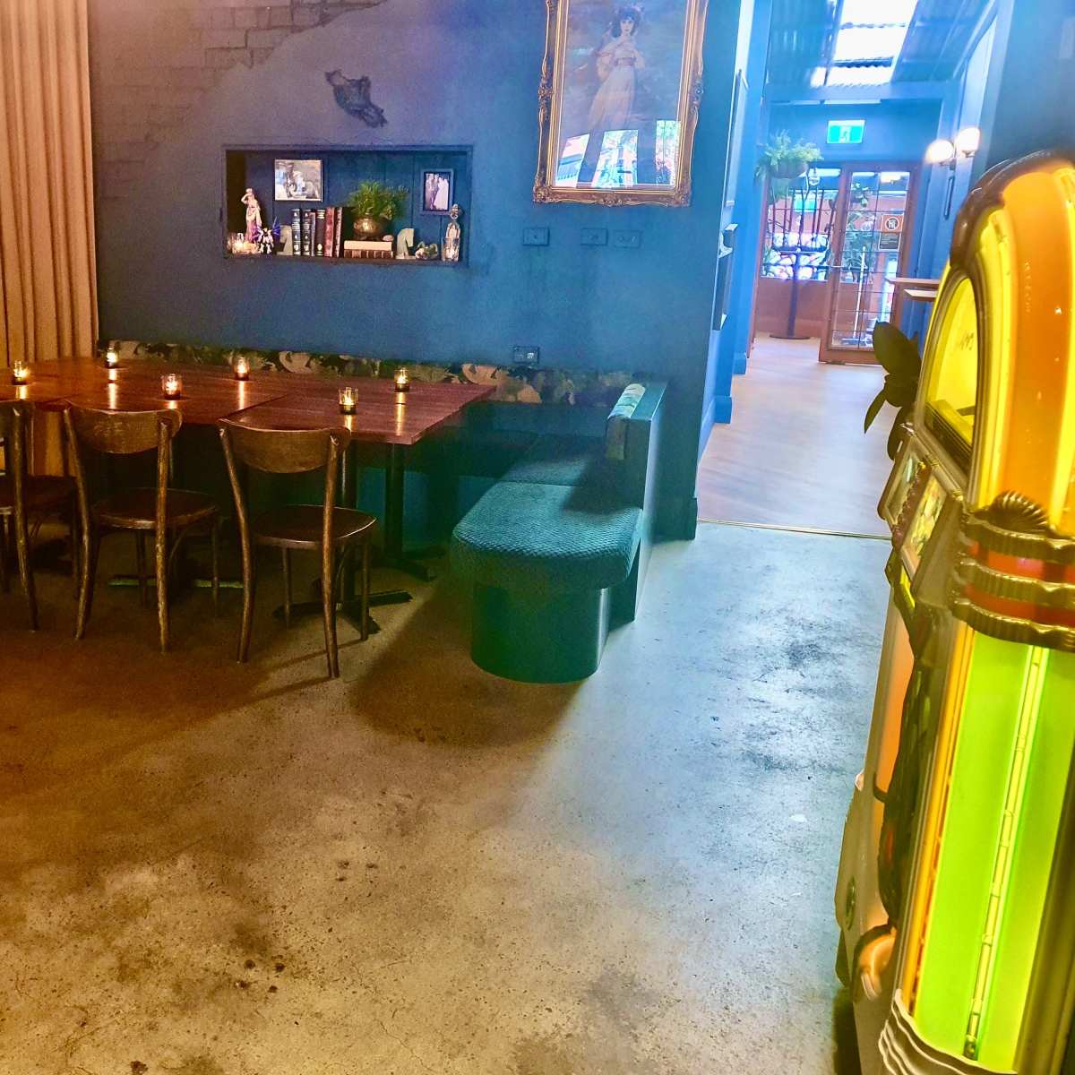 A spacious interior features a large wooden dining table surrounded by chairs, a jukebox in the corner, and textured walls adorned with decor.