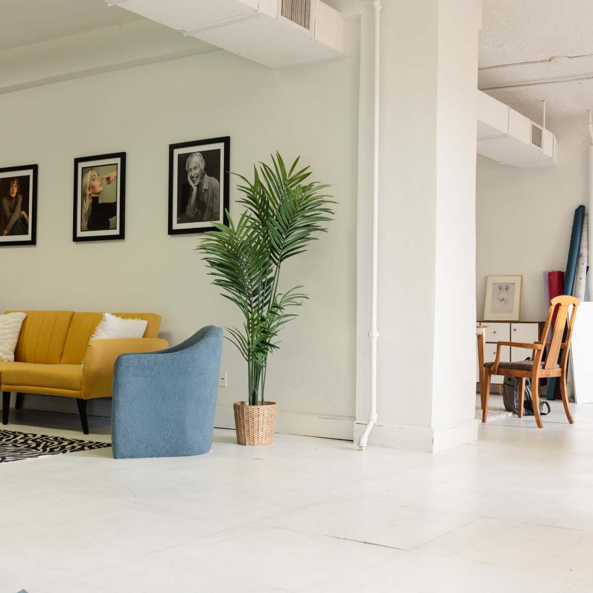 A modern, open studio space with a yellow sofa, blue armchair, and several framed portraits on the walls.