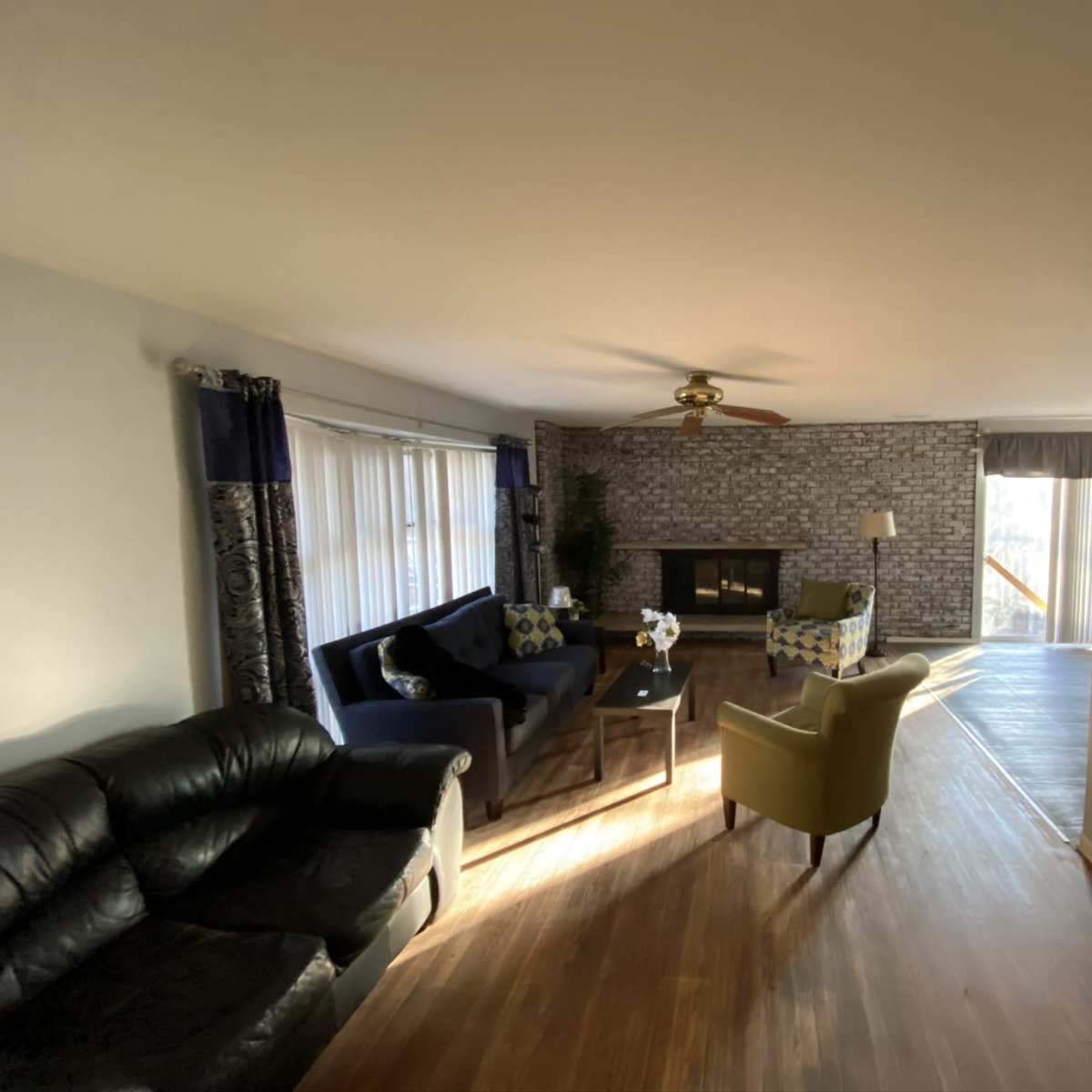 A living room with a black leather sofa, a blue couch with decorative pillows, a coffee table, and a fireplace, illuminated by natural light from large windows.