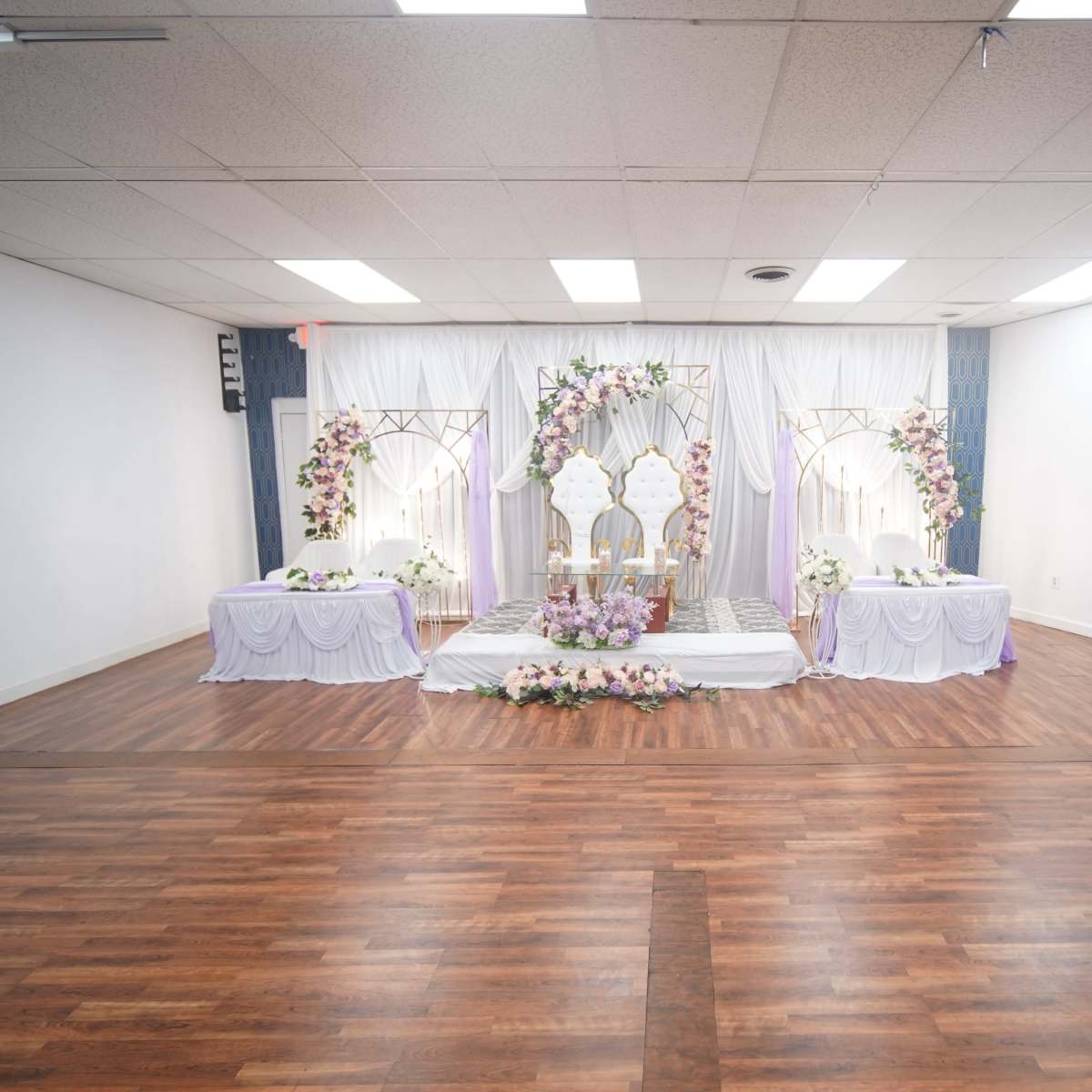 A decorated event space featuring a stage with floral arrangements, a central backdrop, and tables set up for a formal occasion.
