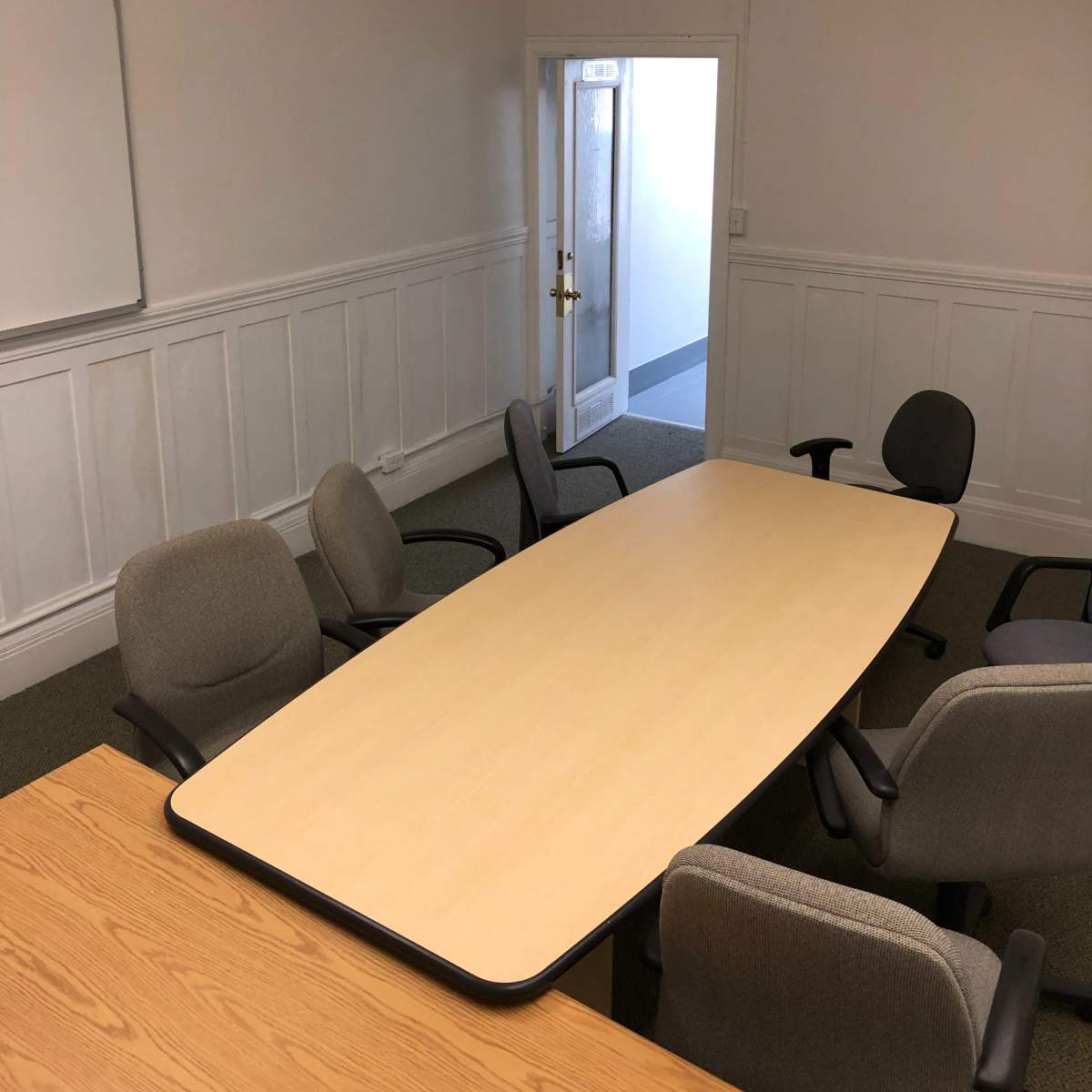 A conference room with a large oval table surrounded by several chairs and a whiteboard on the wall.