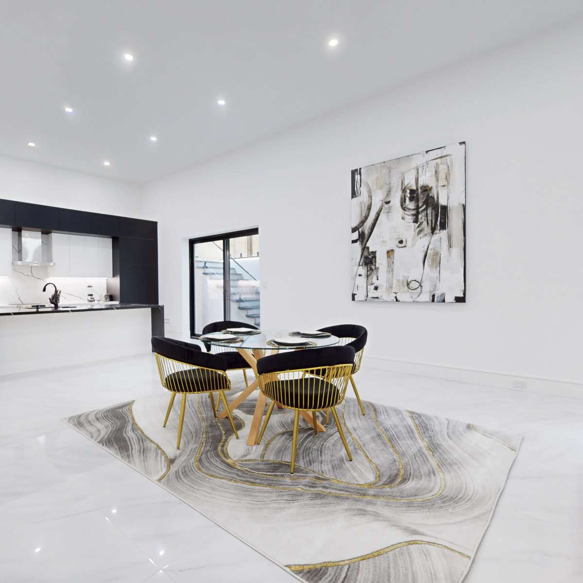 A modern kitchen and dining area featuring a large rug, a round dining table with four chairs, and a background of sleek cabinetry and appliances.