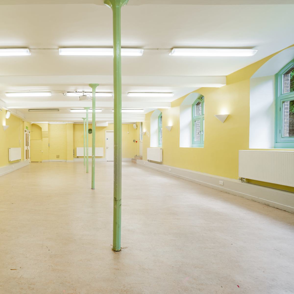 An empty room with yellow walls, a light-colored floor, and green columns supporting the ceiling.