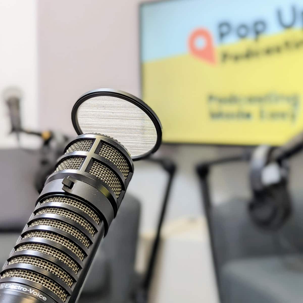 A close-up of a microphone in a podcasting studio with a colorful backdrop displaying "Pop Up Podcasting."