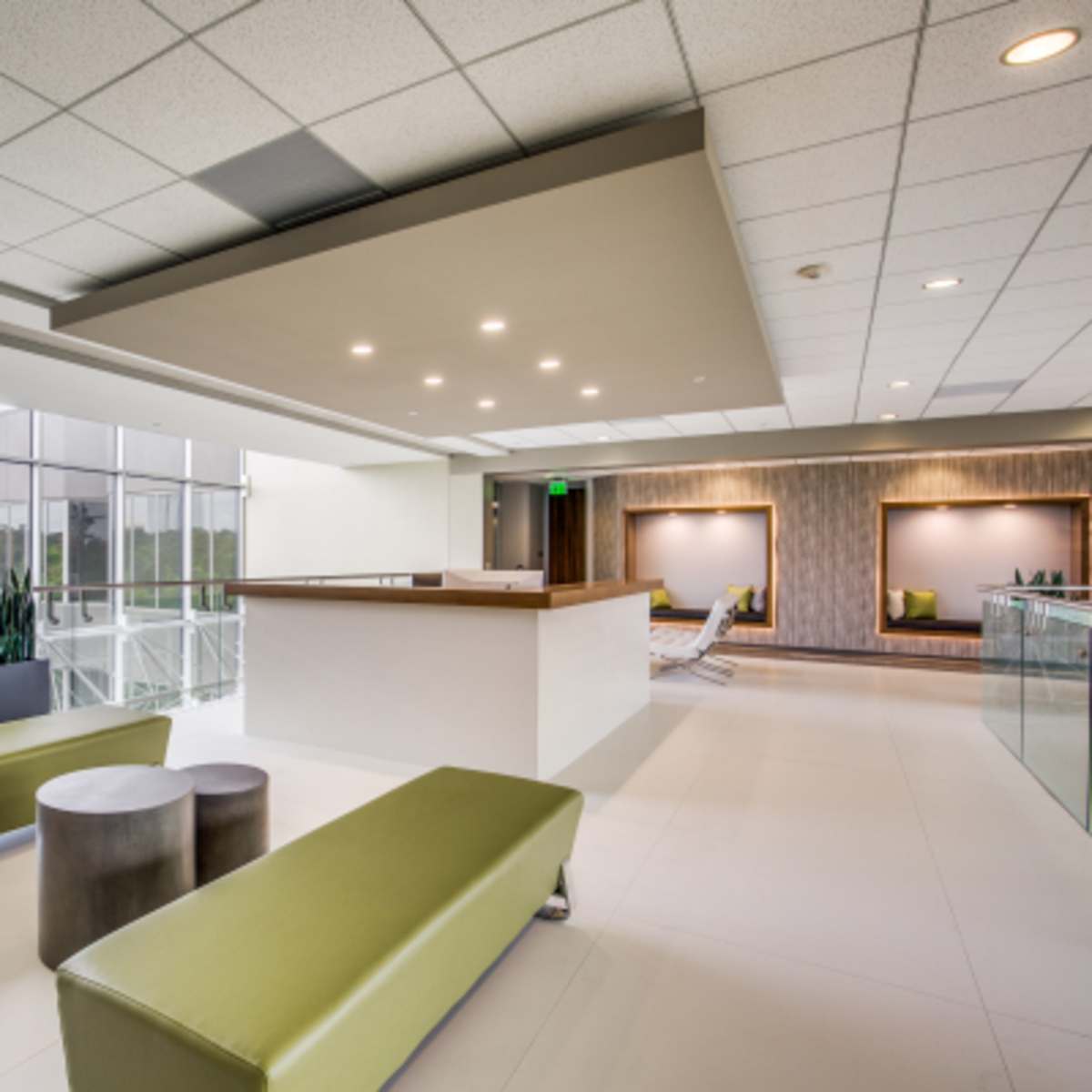 A modern office lobby with green benches, round tables, and large windows overlooking greenery.